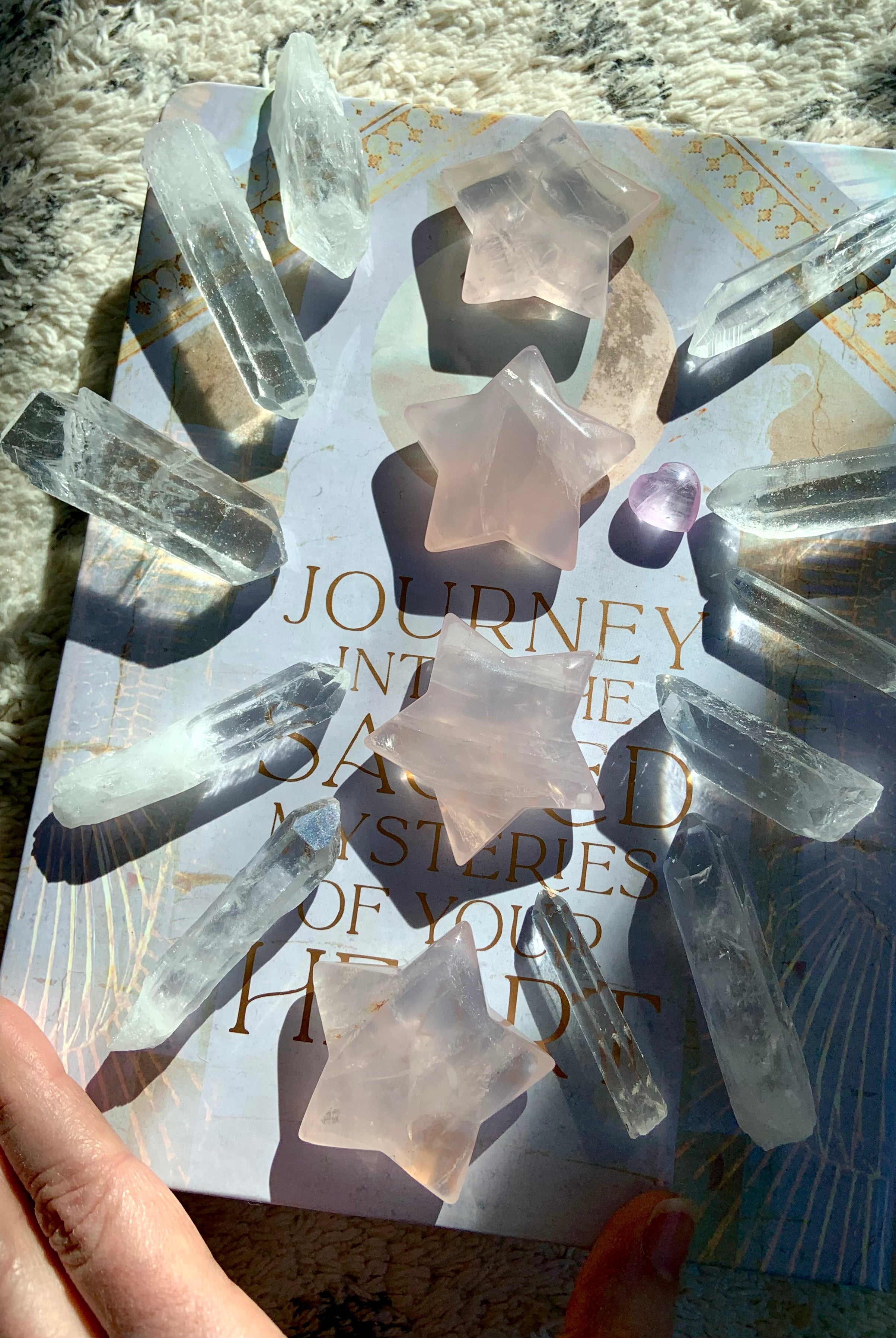 large rose quartz crystal stars with clear quartz points in a sunlit crystal grid on book for heart chakra healing décor