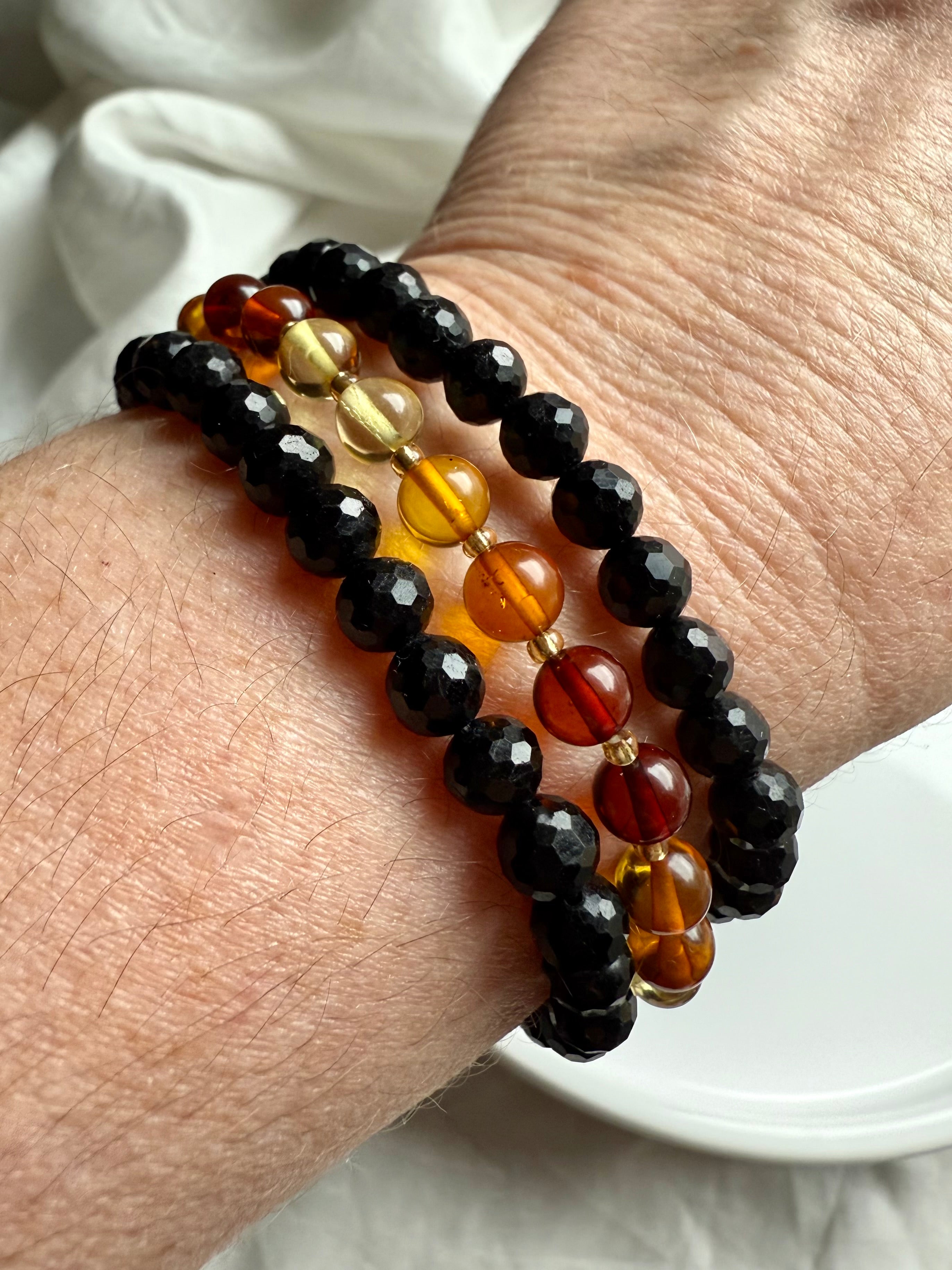black tourmaline paired with golden Baltic amber bracelets for EMF protection, balance, and warmth