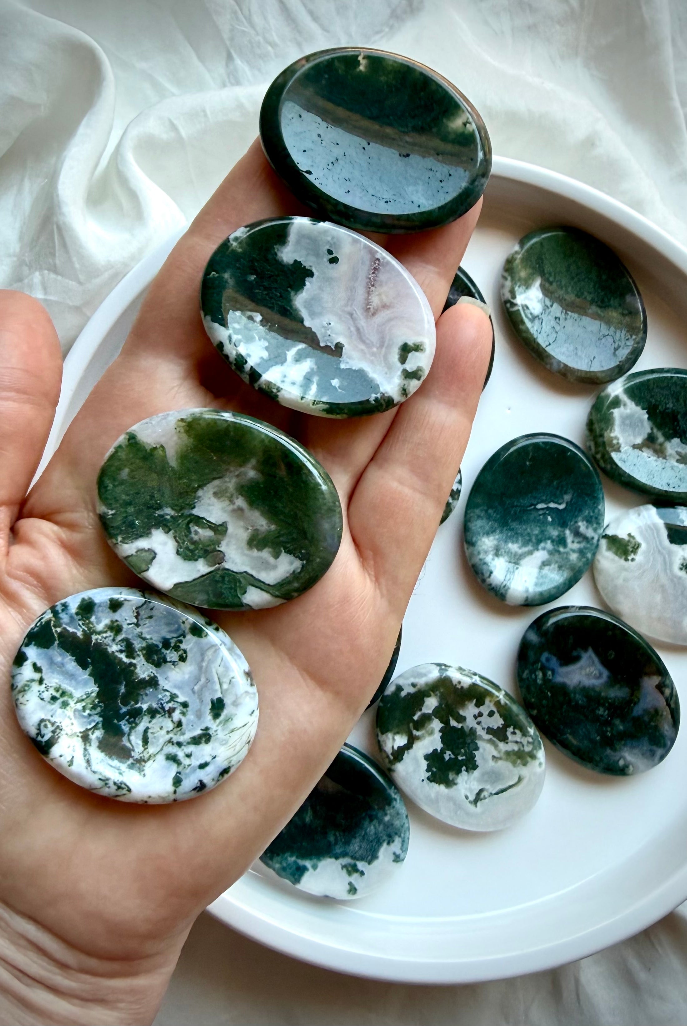 Moss Agate oval worry stone shown on hand with translucent quartz and landscape-like moss inclusions