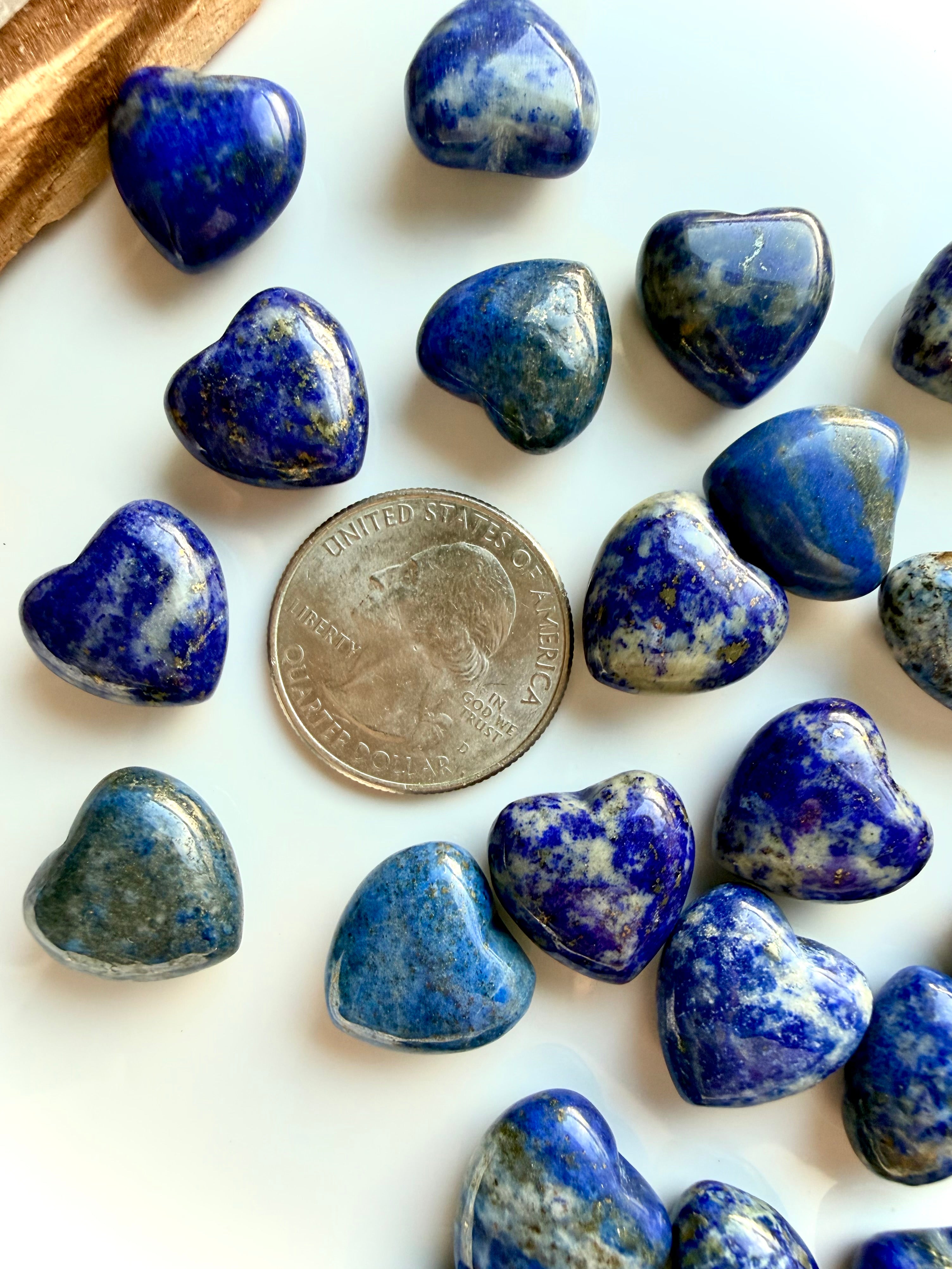 Close-up of Mini Lapis Lazuli heart carvings show with a US quarter for scale, rich blue color, calcite marbling, and subtle pyrite flecks in polished stone