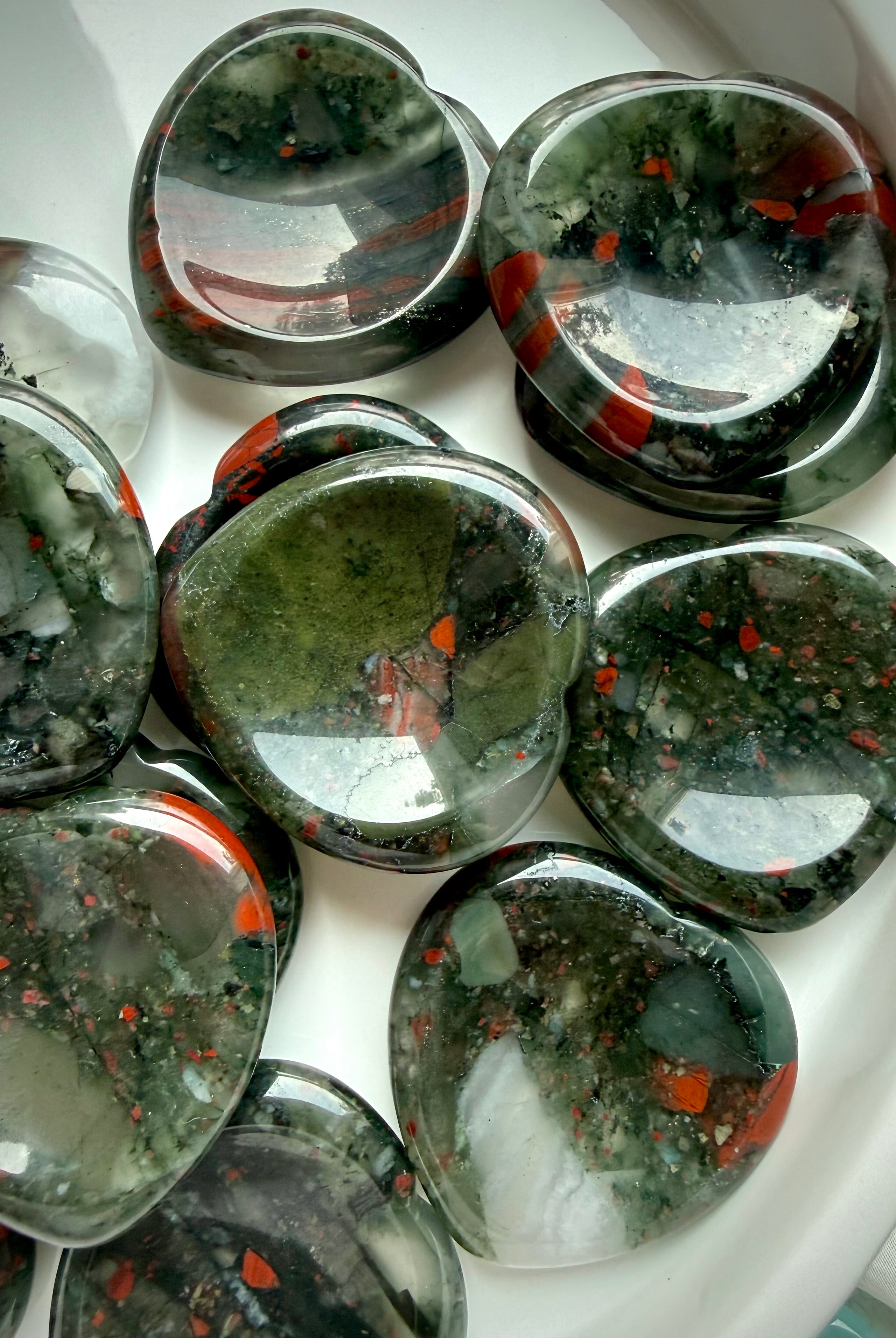 bloodstone heart crystals arranged in ceramic dish, polished worry stones for grounding protection and steady energy
