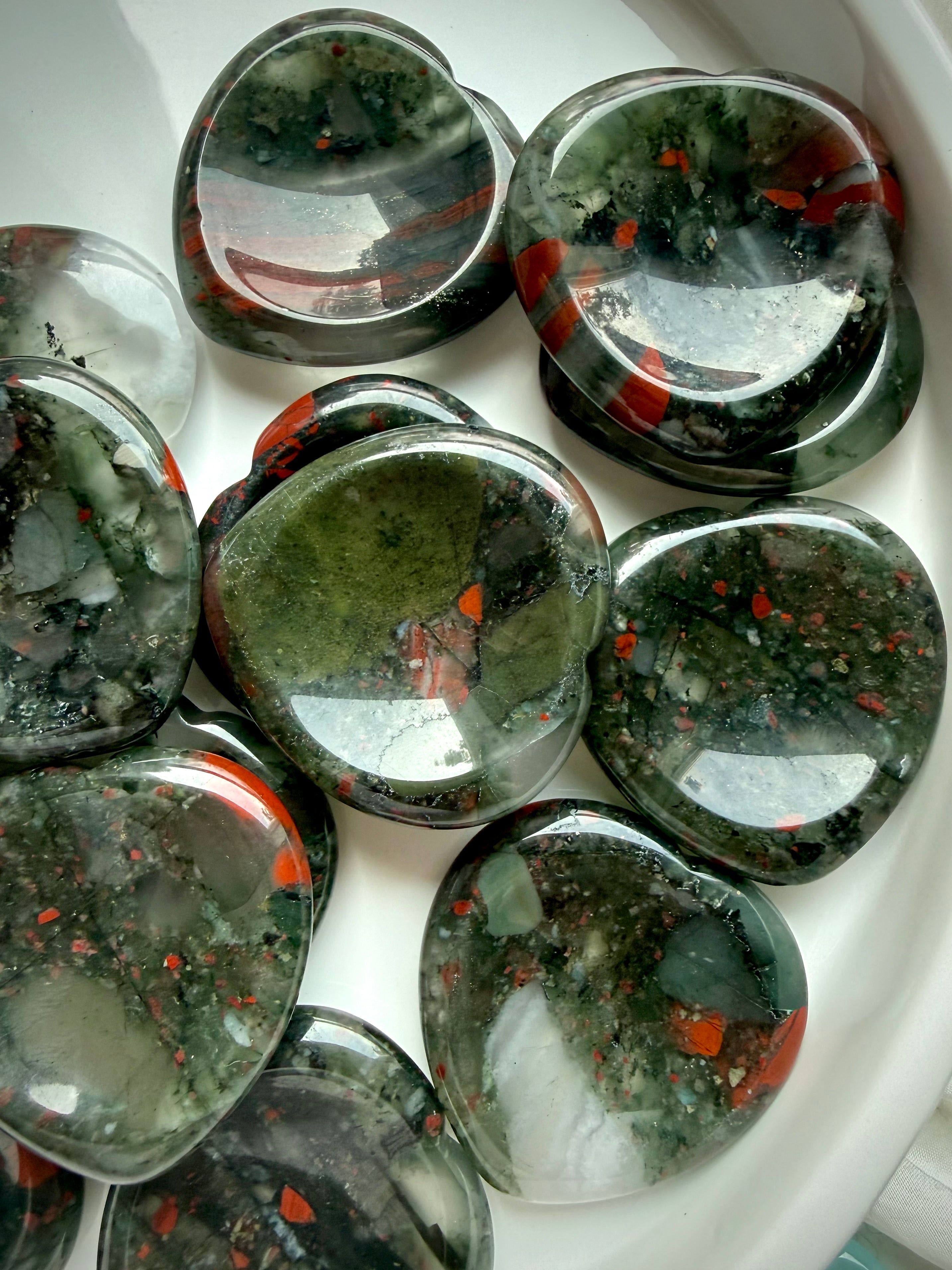 bloodstone heart crystals arranged in ceramic dish, polished worry stones for grounding protection and steady energy