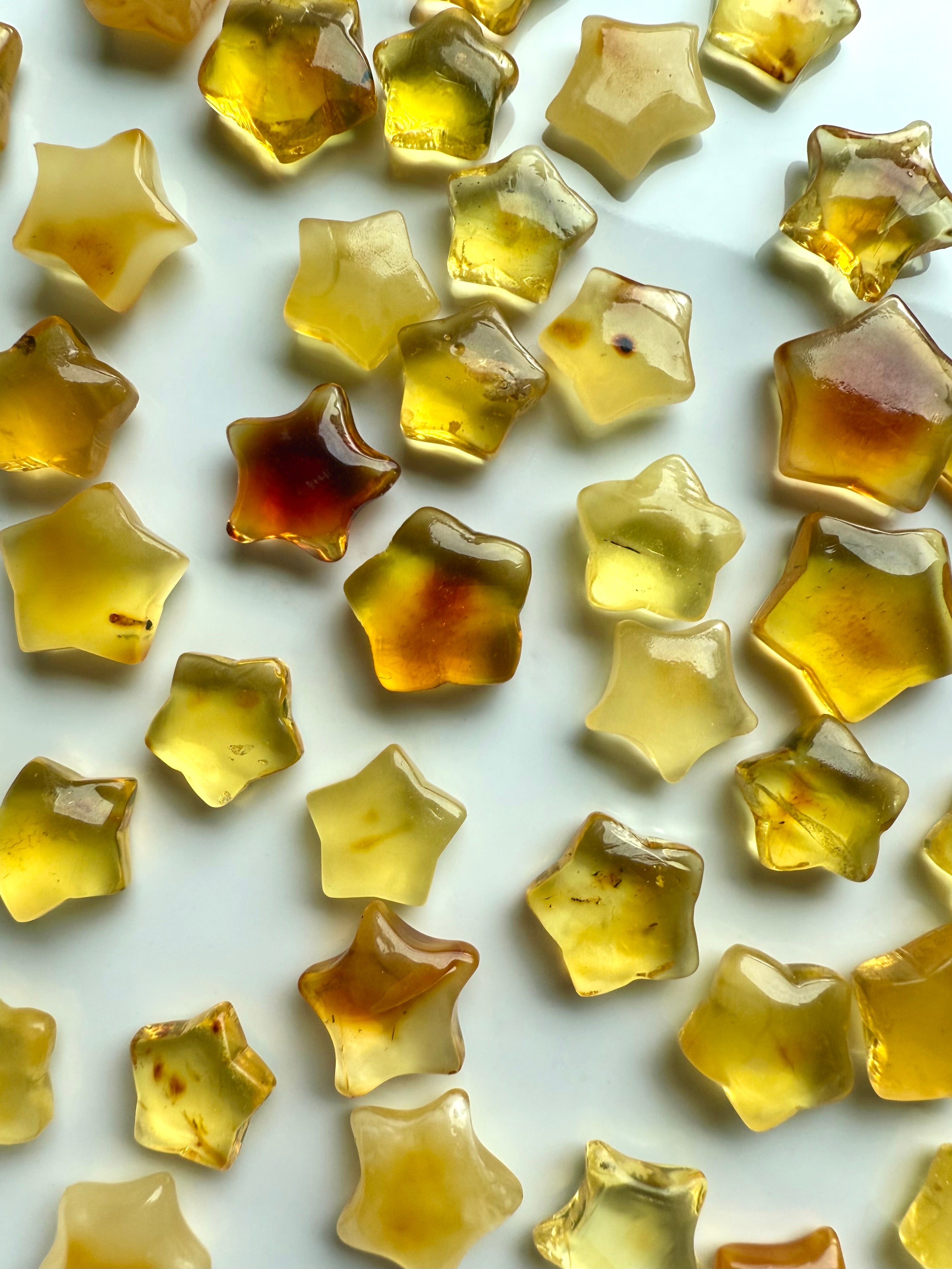 Baltic Amber star carvings with natural inclusions in golden honey tones on a white background — healing crystal stars for the Solar Plexus chakra, vitality, and protection.