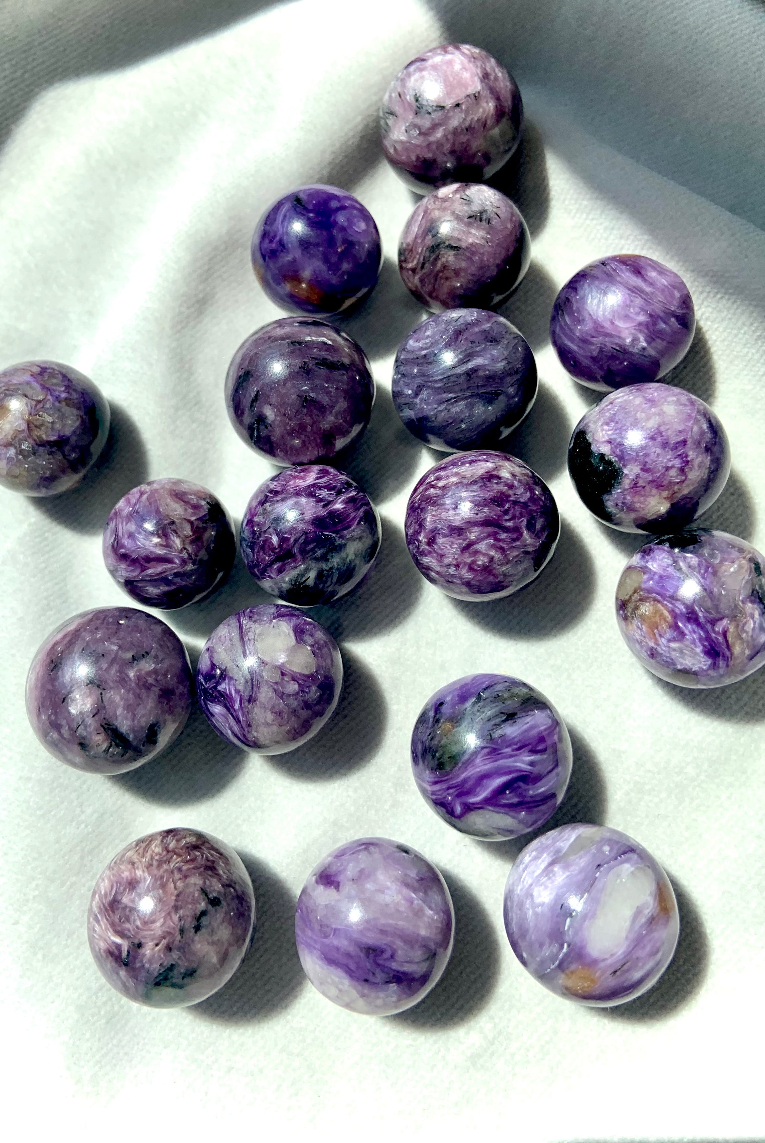 An array of Purple Charoite mini spheres photographed in bright natural light on a light background