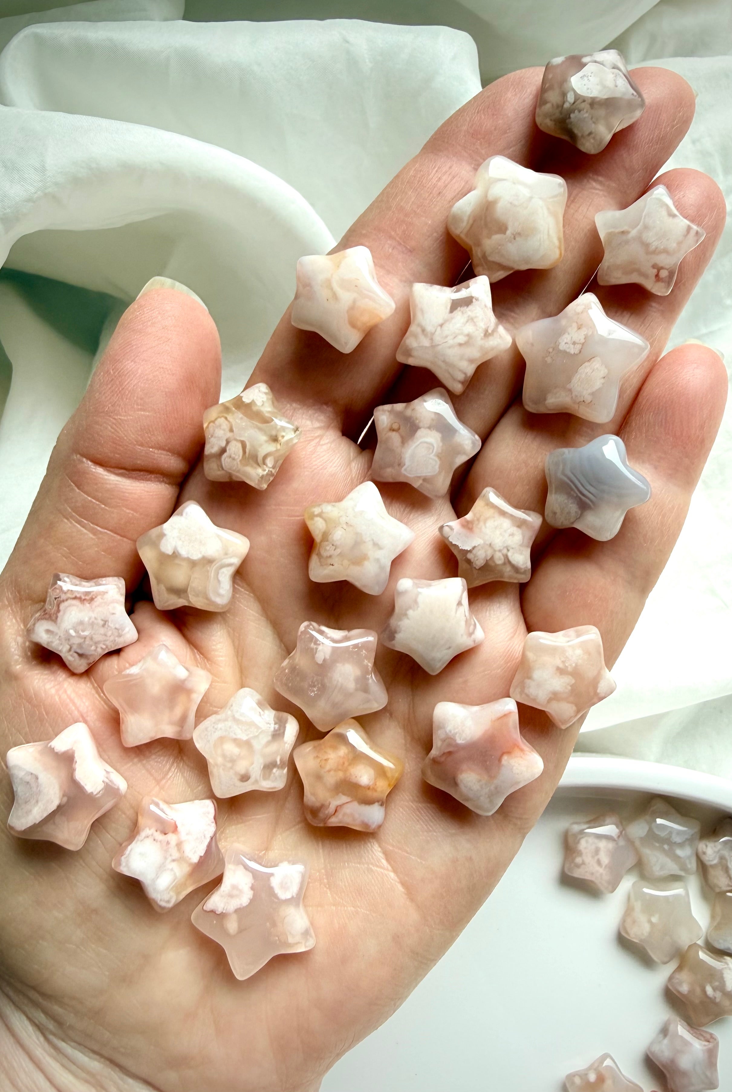 Hand holding mini Flower Agate star carvings with floral inclusions and dreamy pastel chalcedony tones