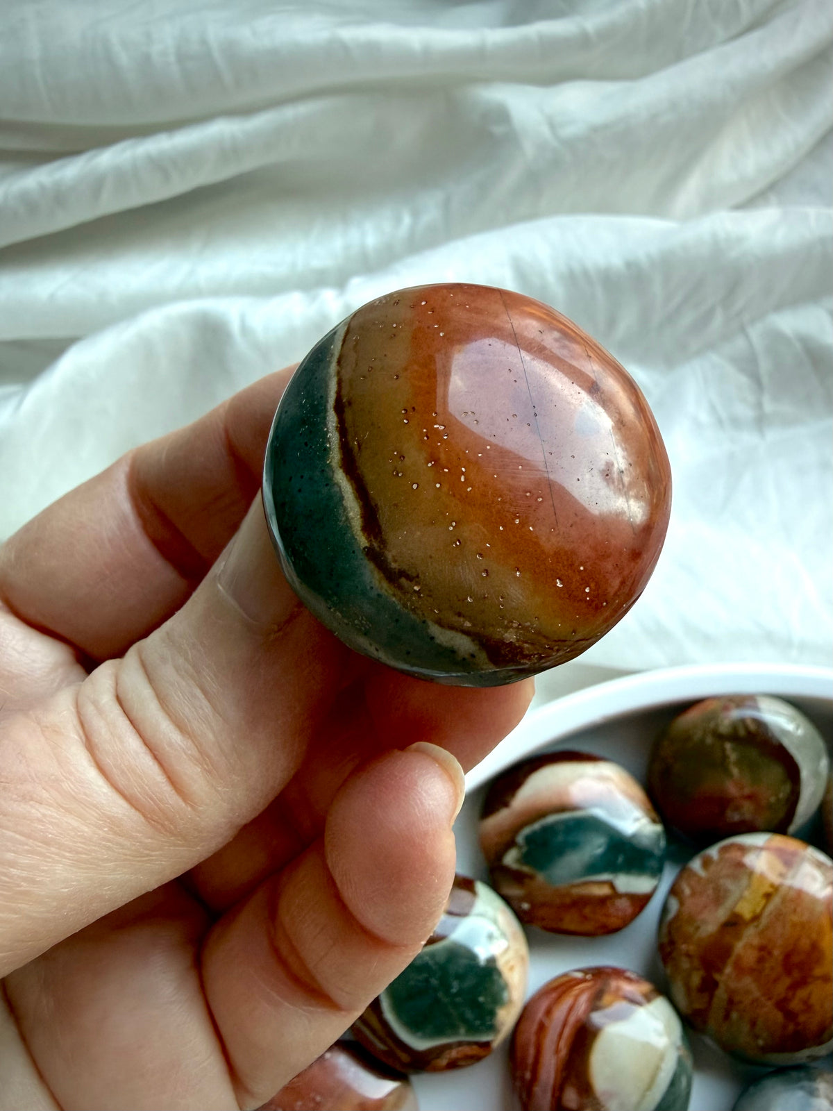 Closeup of a mini Polychrome Jasper palm stone with earthy green, terracotta, gray & cream patterns