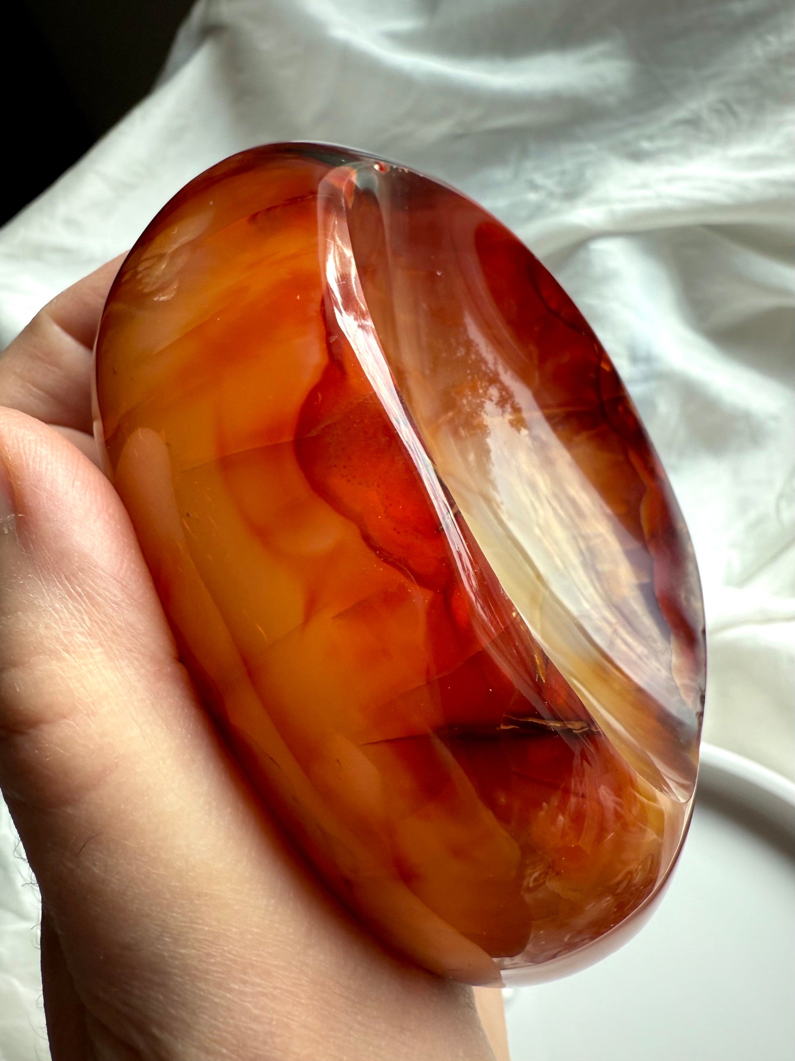 Polished Carnelian crystal bowl held in hand, showing fiery orange, red, and white banded interior.