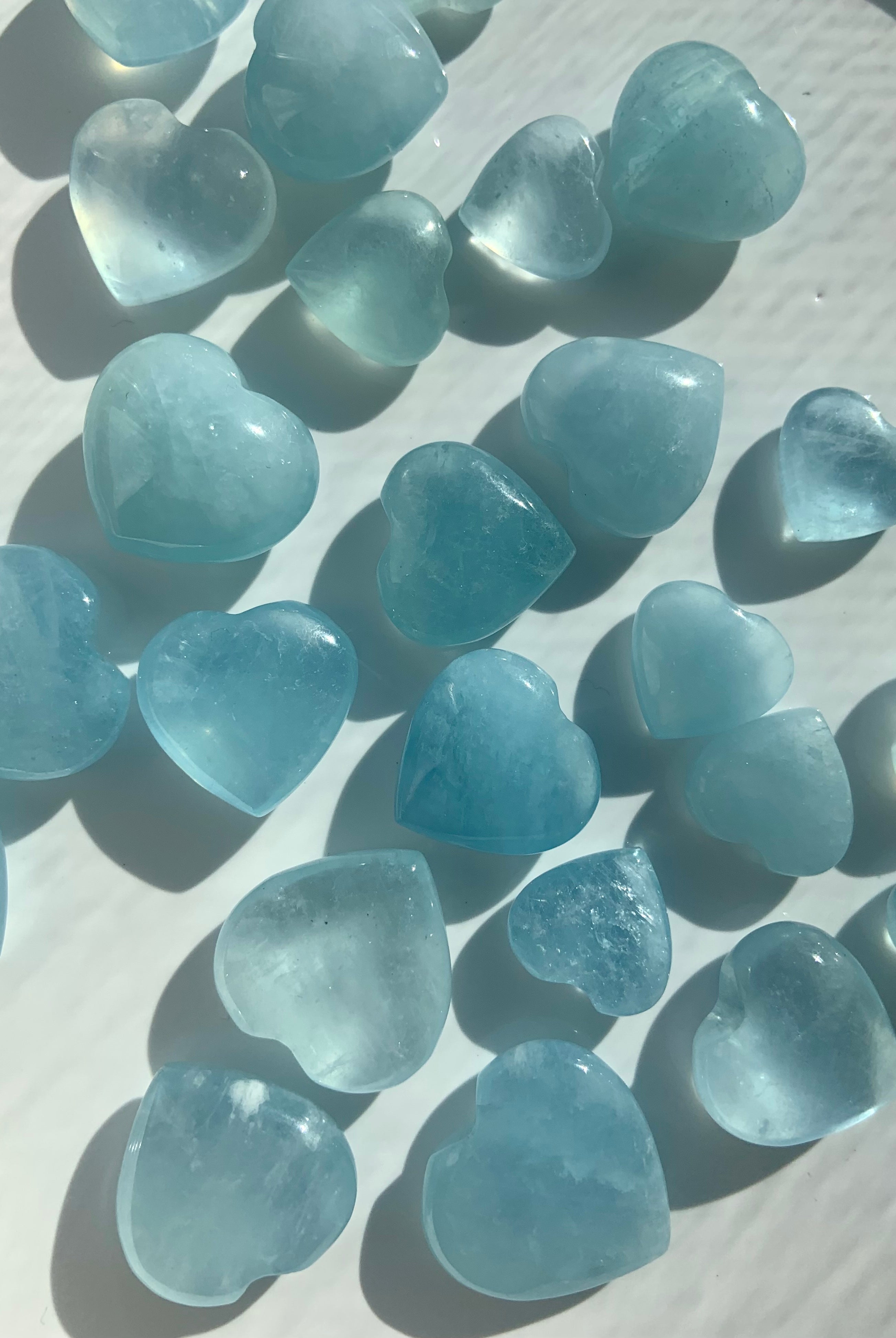 Closeup of Aquamarine crystal hearts on a white background — mini heart carvings in serene blue tones for calm, clarity + throat chakra support.