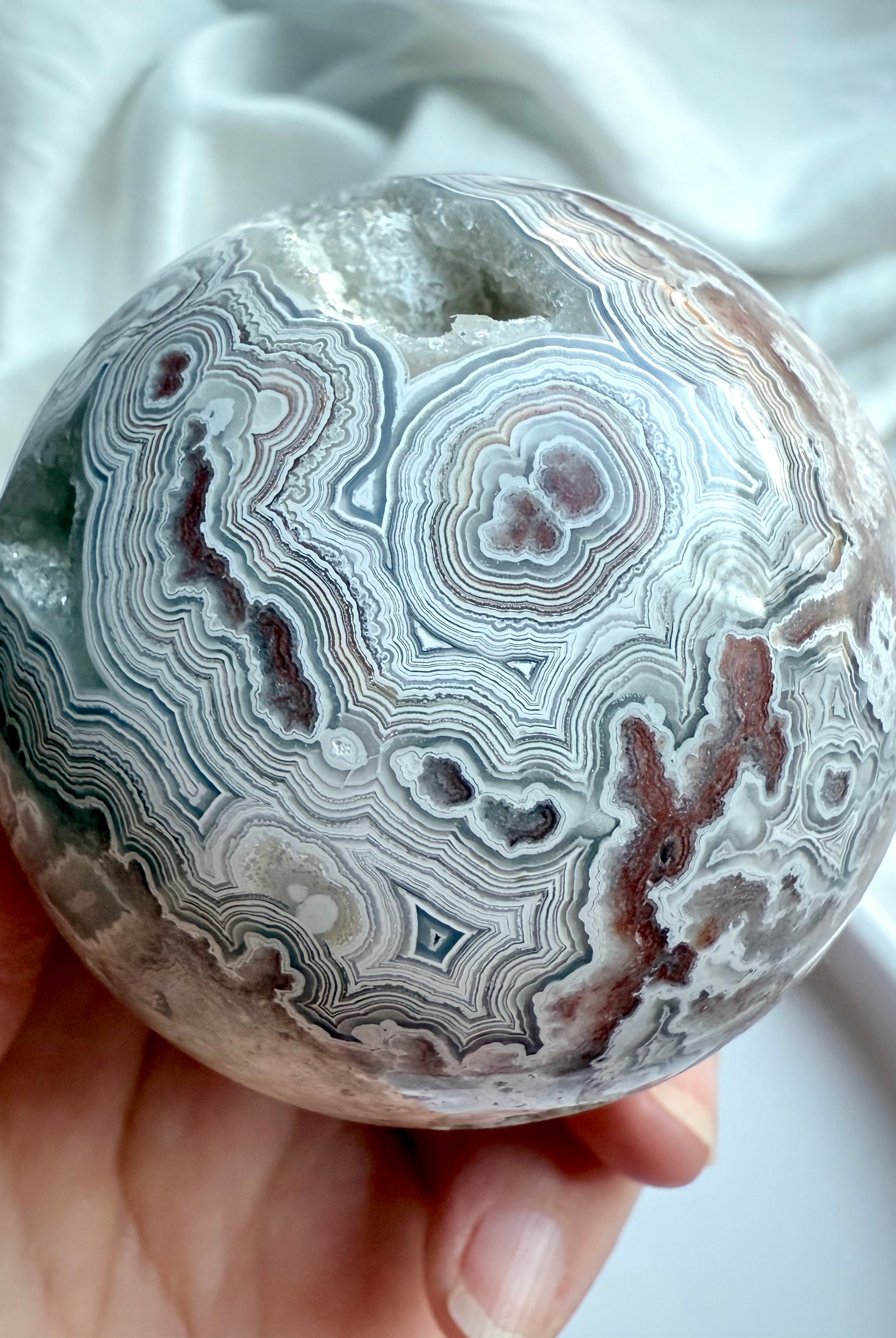 Detailed view of unique lace agate orb featuring bullseye patterns and geode inclusions, hand holding sphere