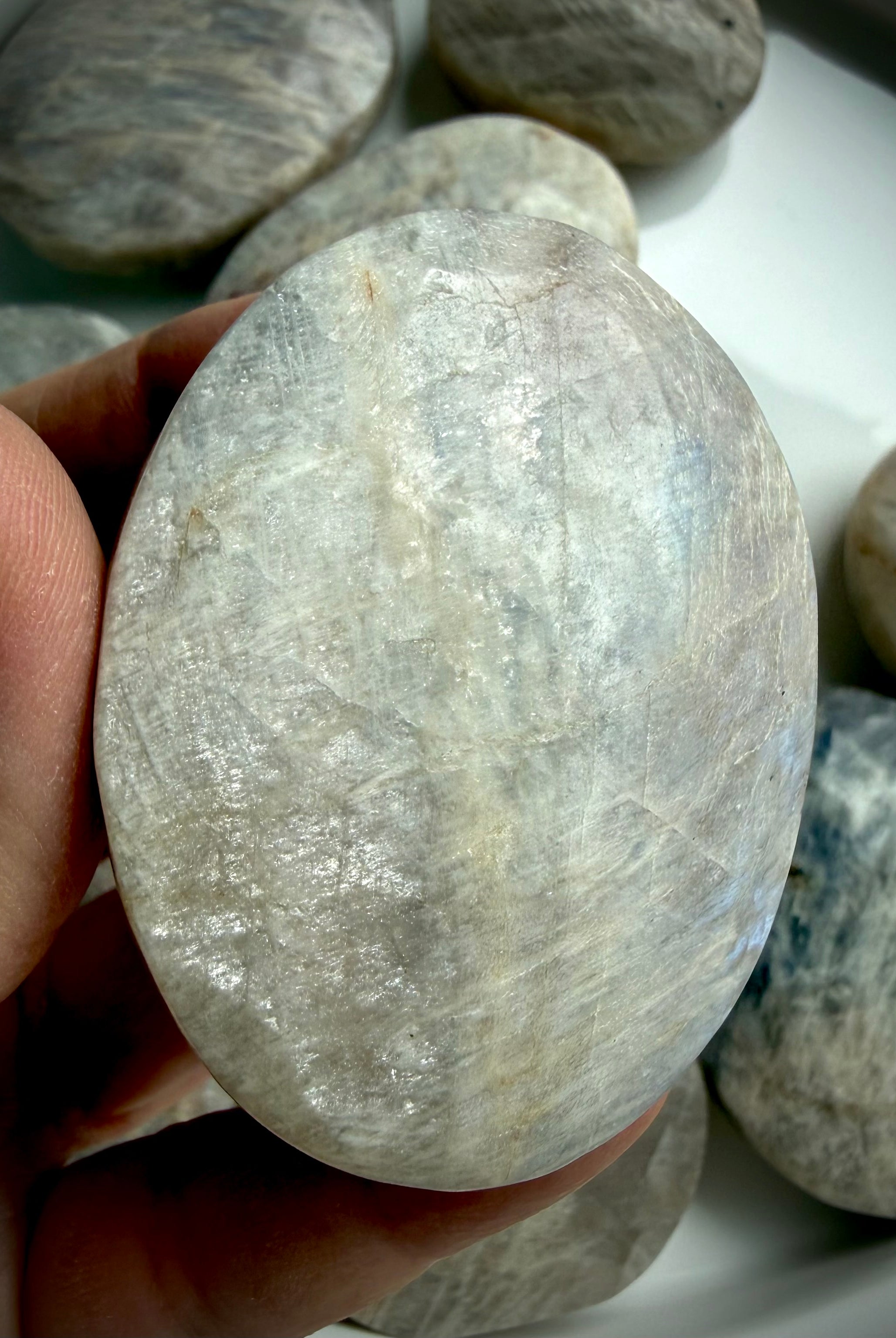 polished moonstone palm stone with silver-white flash and subtle blue iridescence
