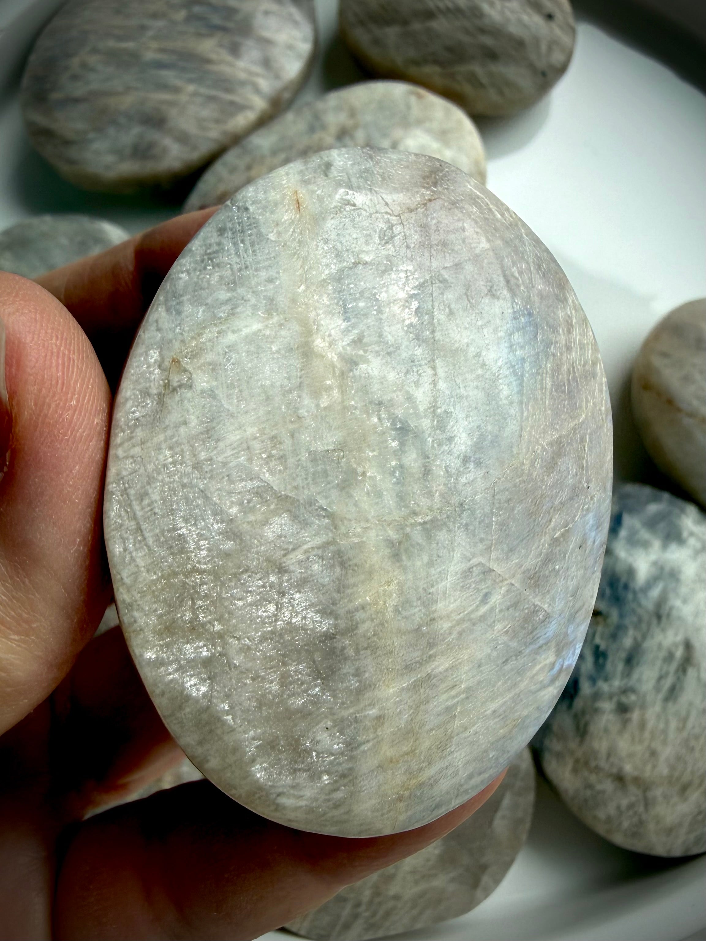 polished moonstone palm stone with silver-white flash and subtle blue iridescence