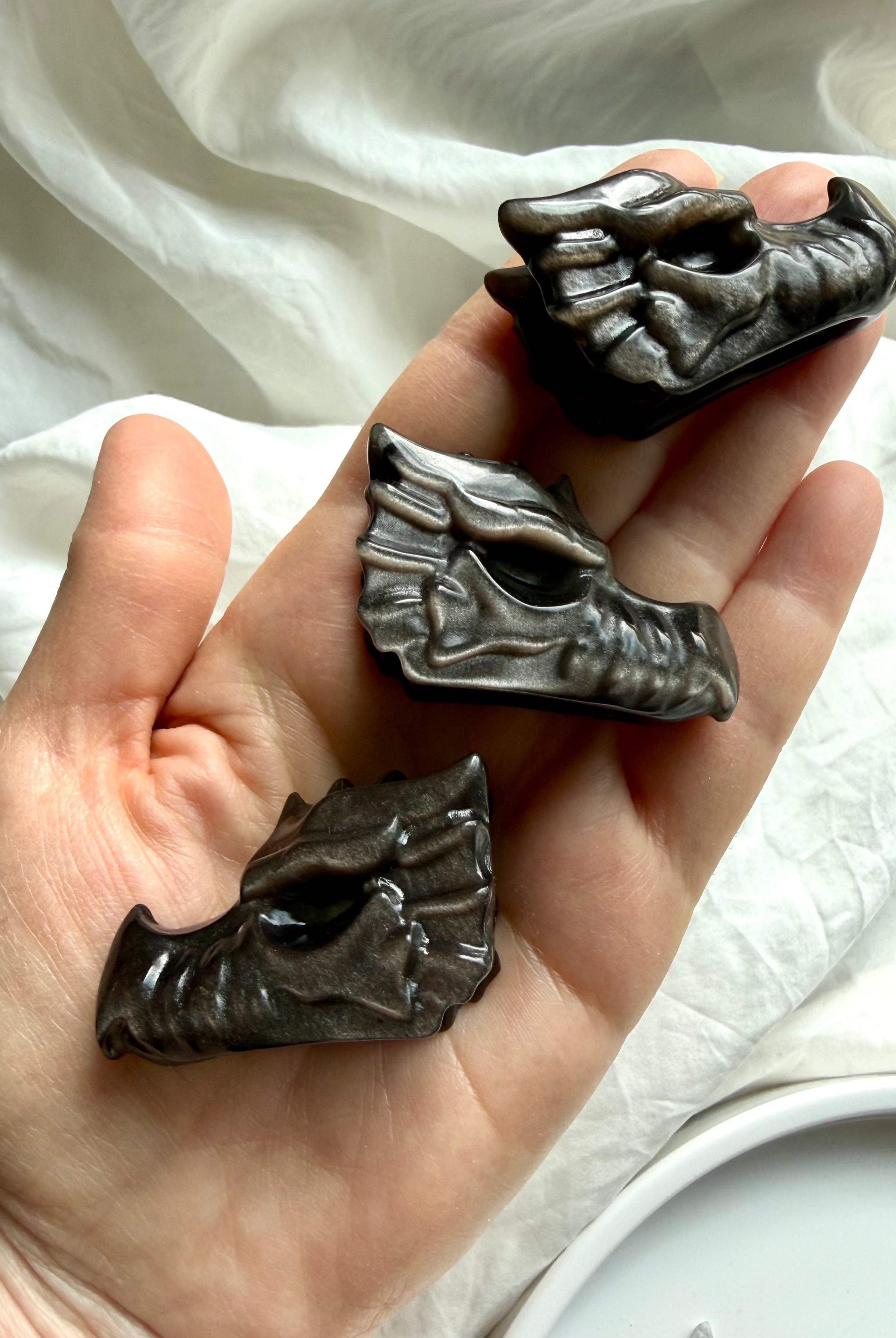 hand holding three silver sheen obsidian dragon carvings showing detailed carved texture, protective crystal for strength and transformation