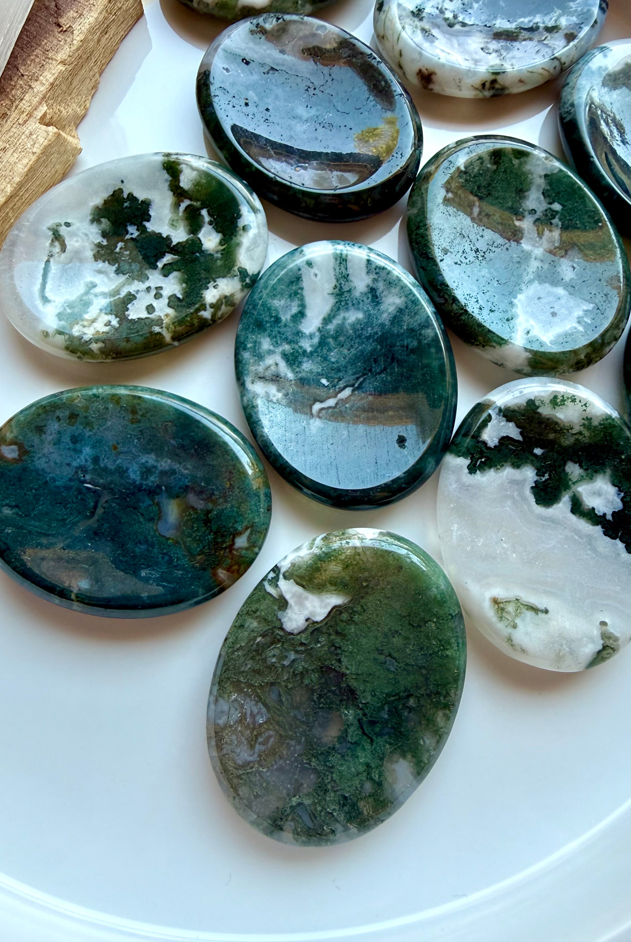 Assorted Moss Agate oval worry stones displayed on a white plate with natural moss patterns and polished finish