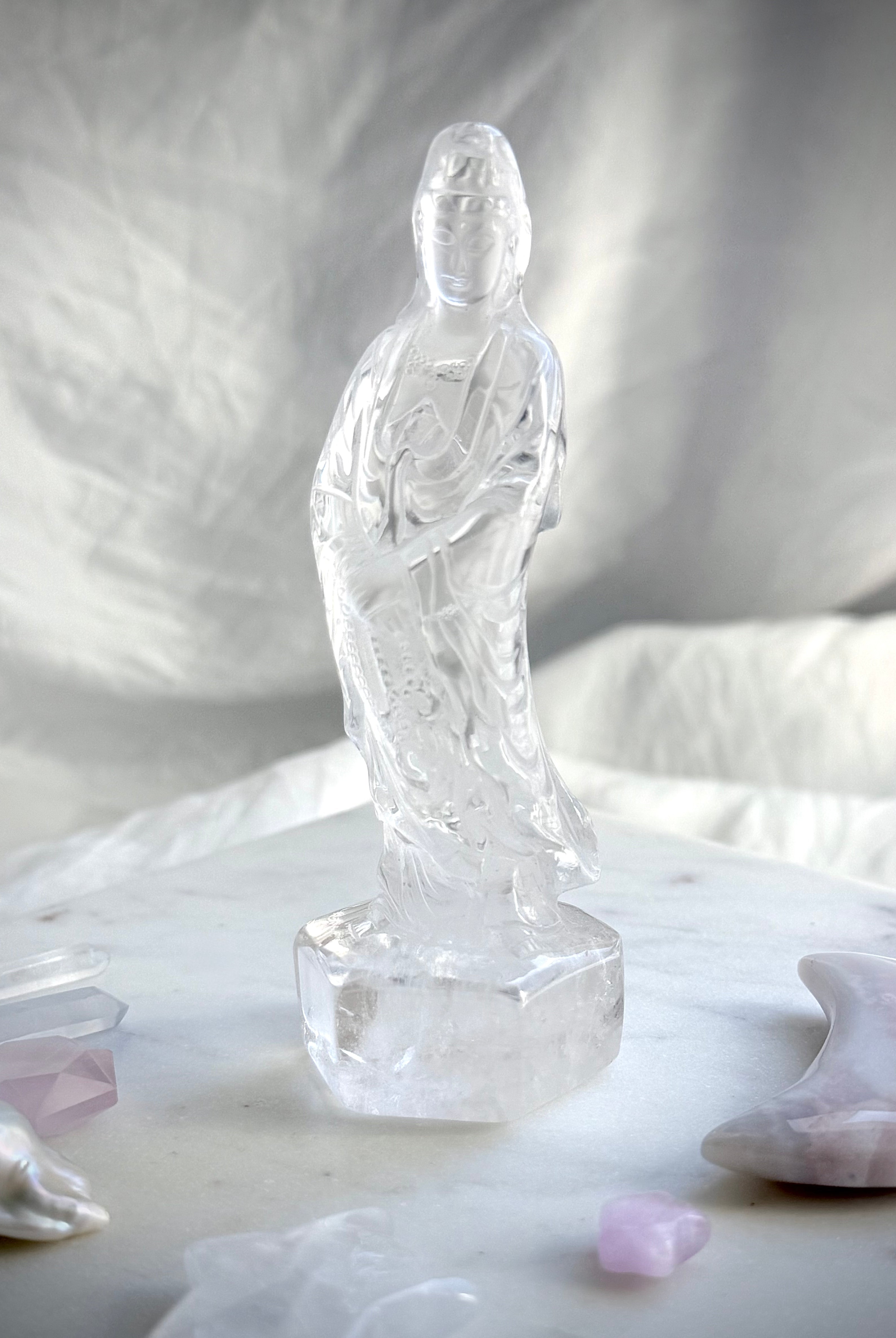 Hand-carved Clear Quartz Quan Yin figurine surrounded by crystals and soft altar décor