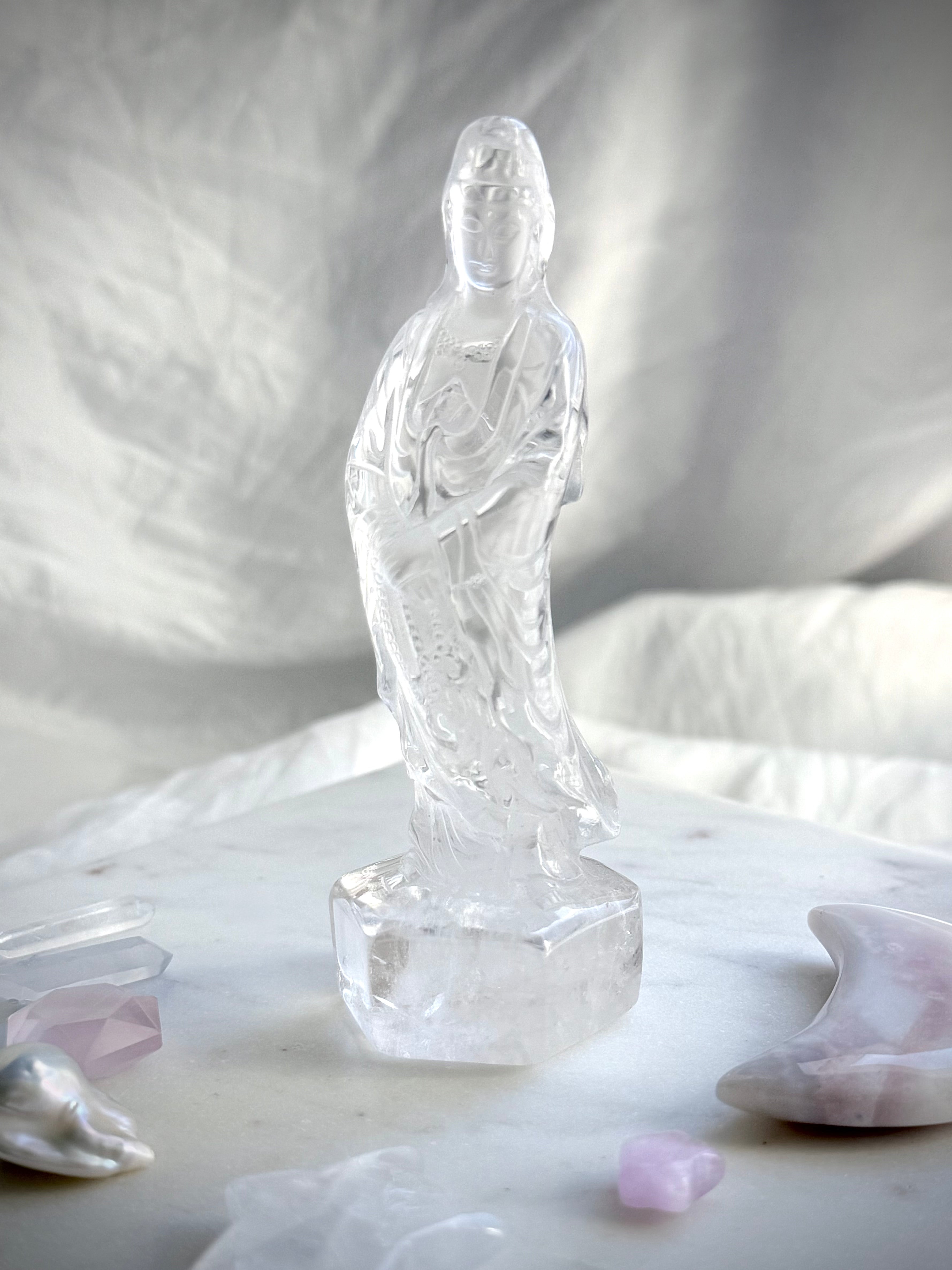Hand-carved Clear Quartz Quan Yin figurine surrounded by crystals and soft altar décor