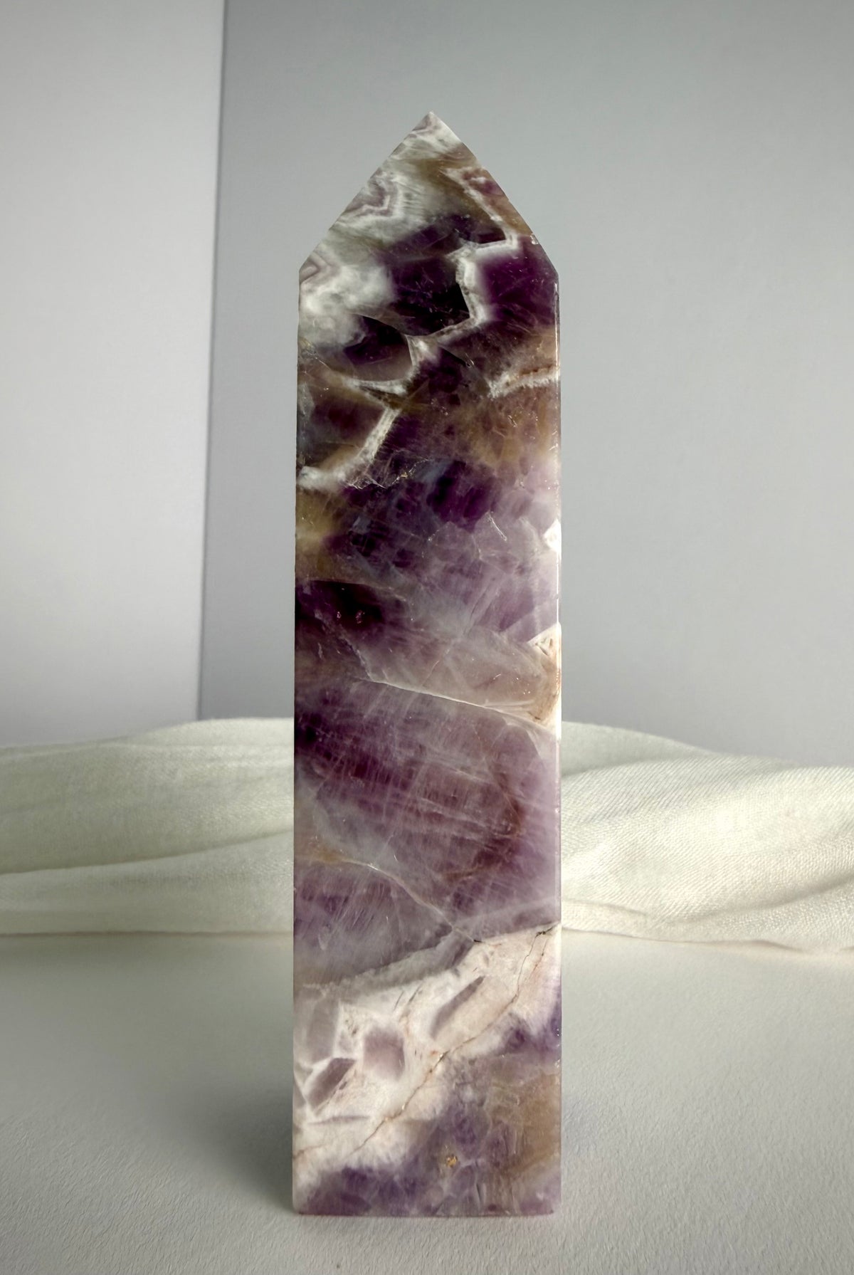 Polished Dream Amethyst tower standing upright, featuring rich purple crystal formations, white quartz chevrons and natural smoky tones