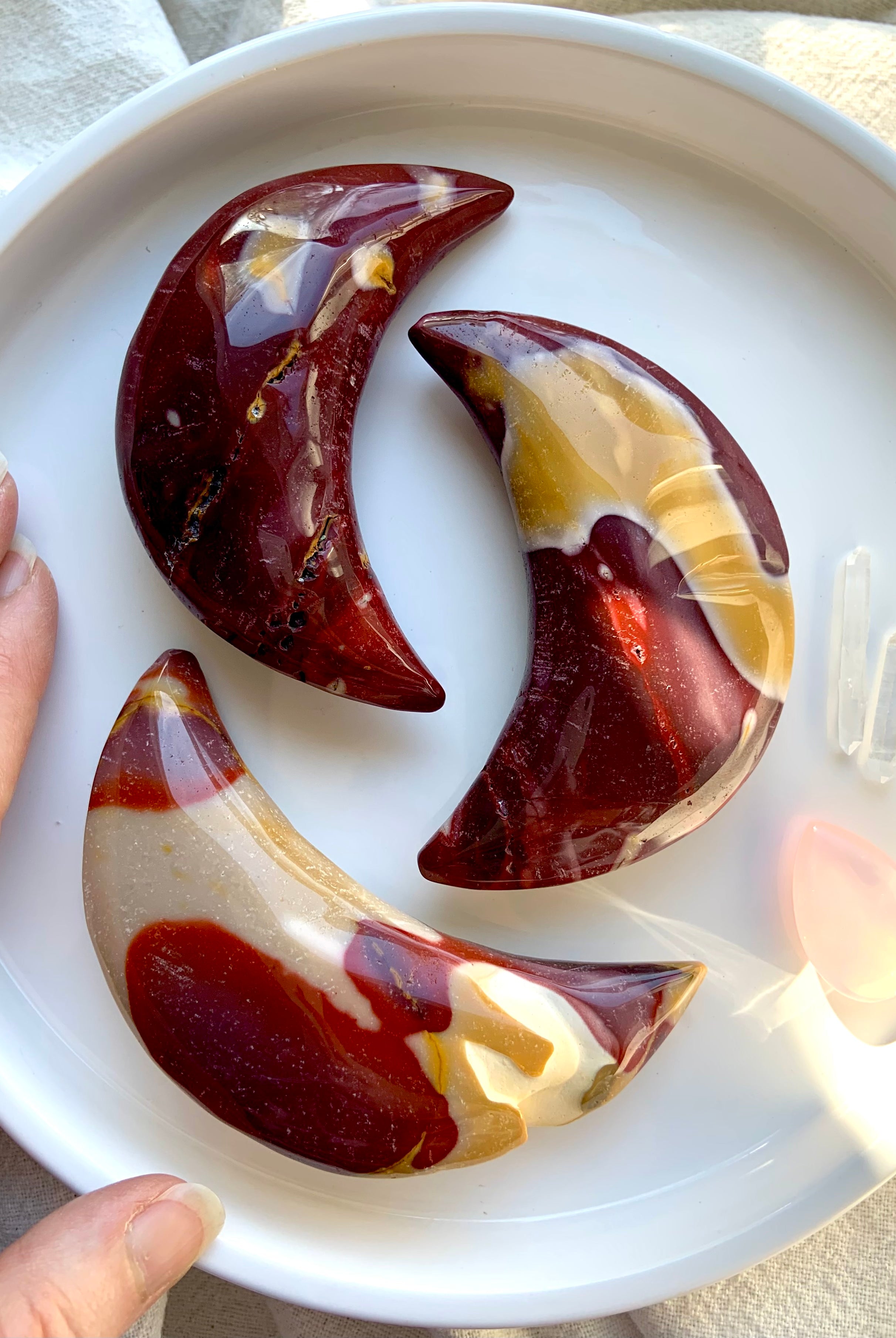 Palm sized, hand carved Mookaite Jasper Crescent Moons shown on a white background with my hand for scale. Choose your favorite!