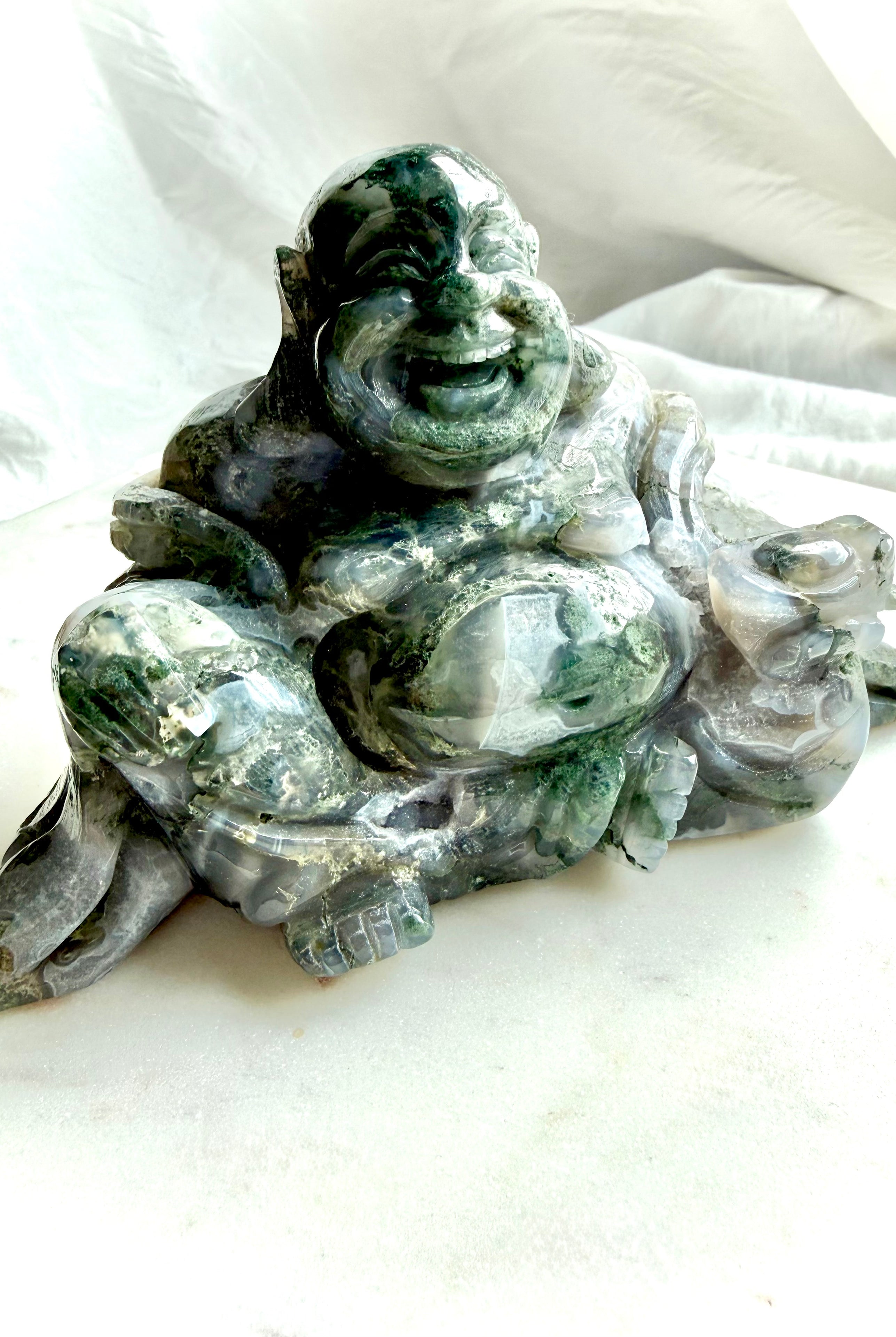 Side view of a Large Moss Agate Laughing Buddha crystal carving with translucent Moss Agate