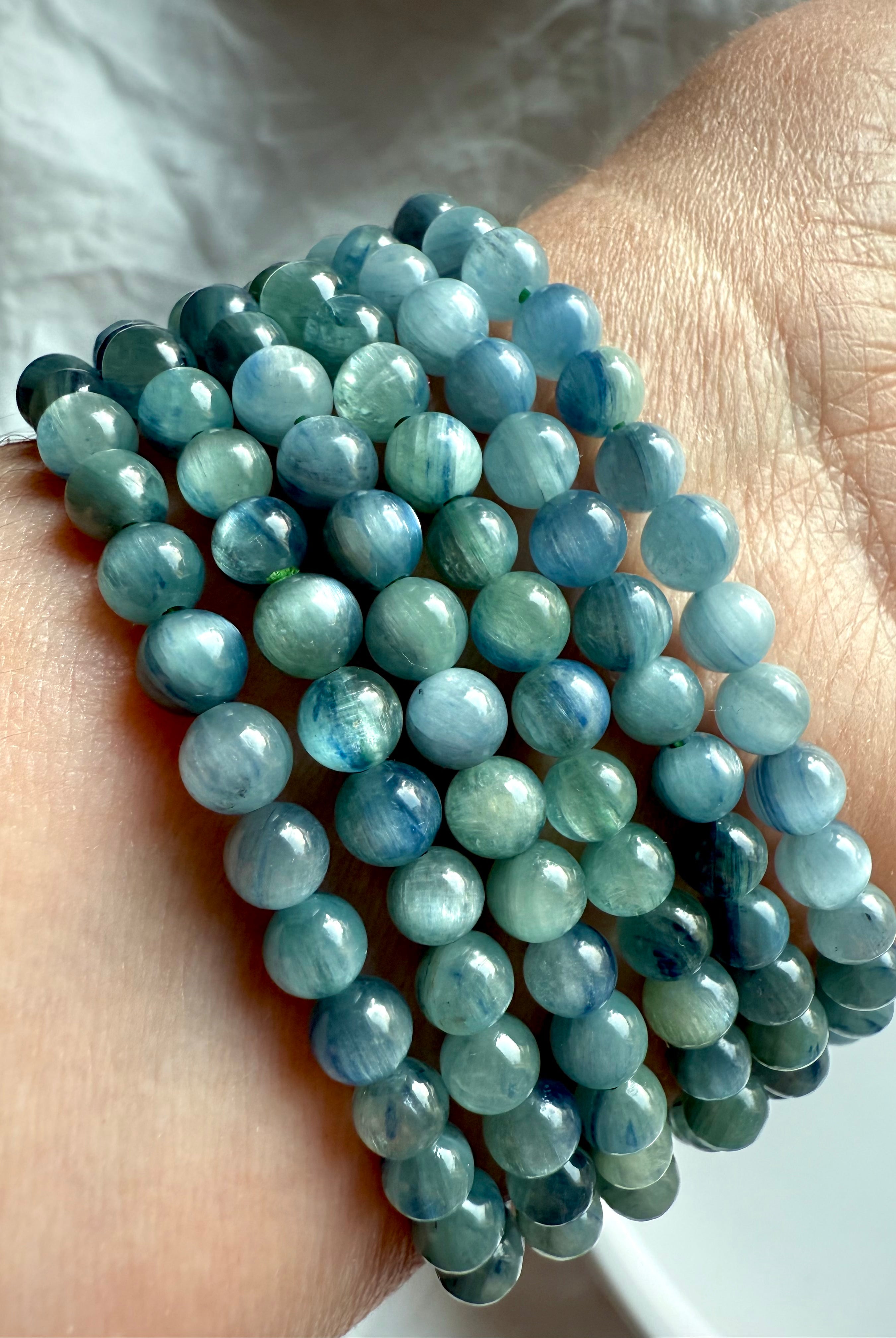 close-up of stacked blue-green kyanite bracelets showing natural silky chatoyance and layered blue tones for throat chakra healing