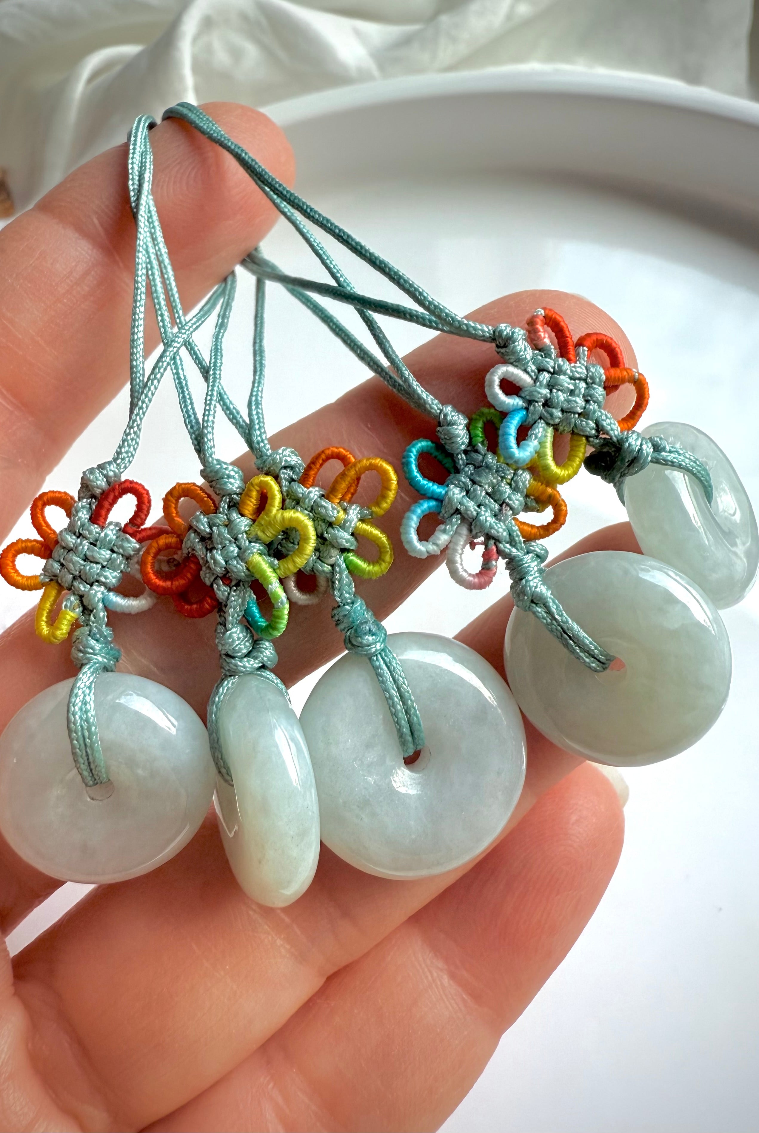 Hand holding five jade peace buckle pendants with colorful macrame knotwork on green cord