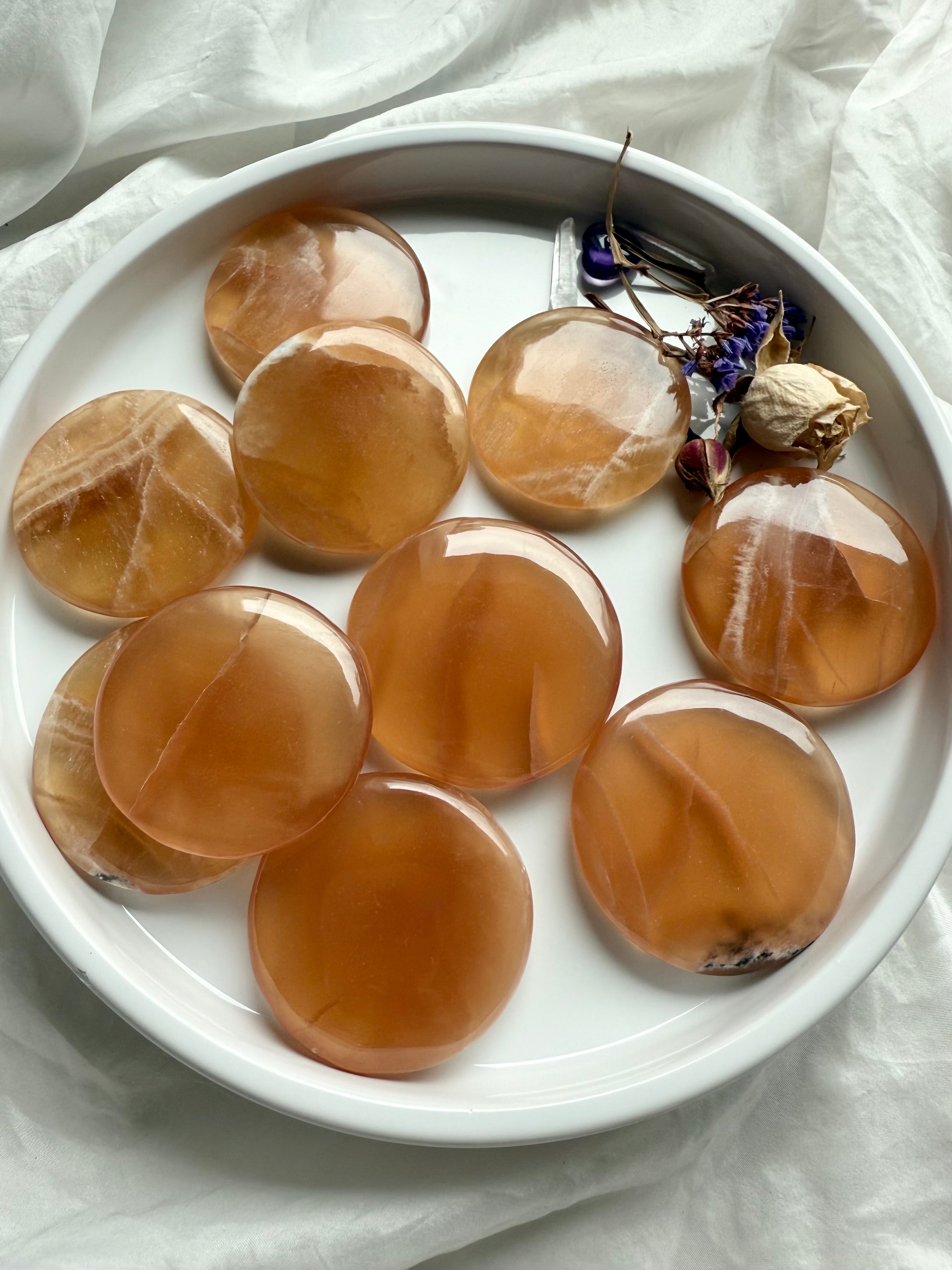 Top-down view of Honey Calcite meditation stones arranged in a white dish with dried flowers for ritual use and gentle empowerment.