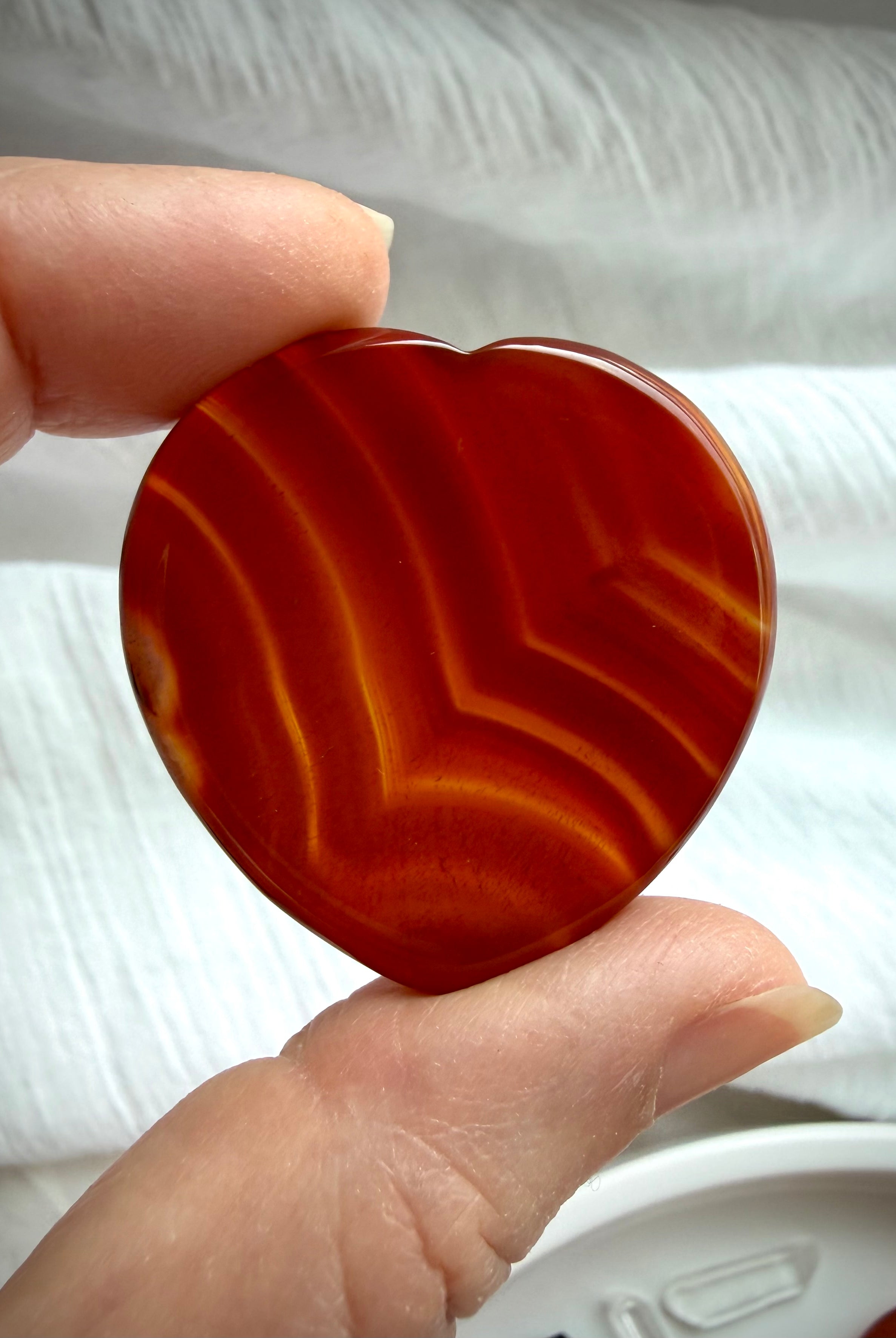 Translucent Carnelian heart worry stone with vivid red-orange banding and polished thumb indentation