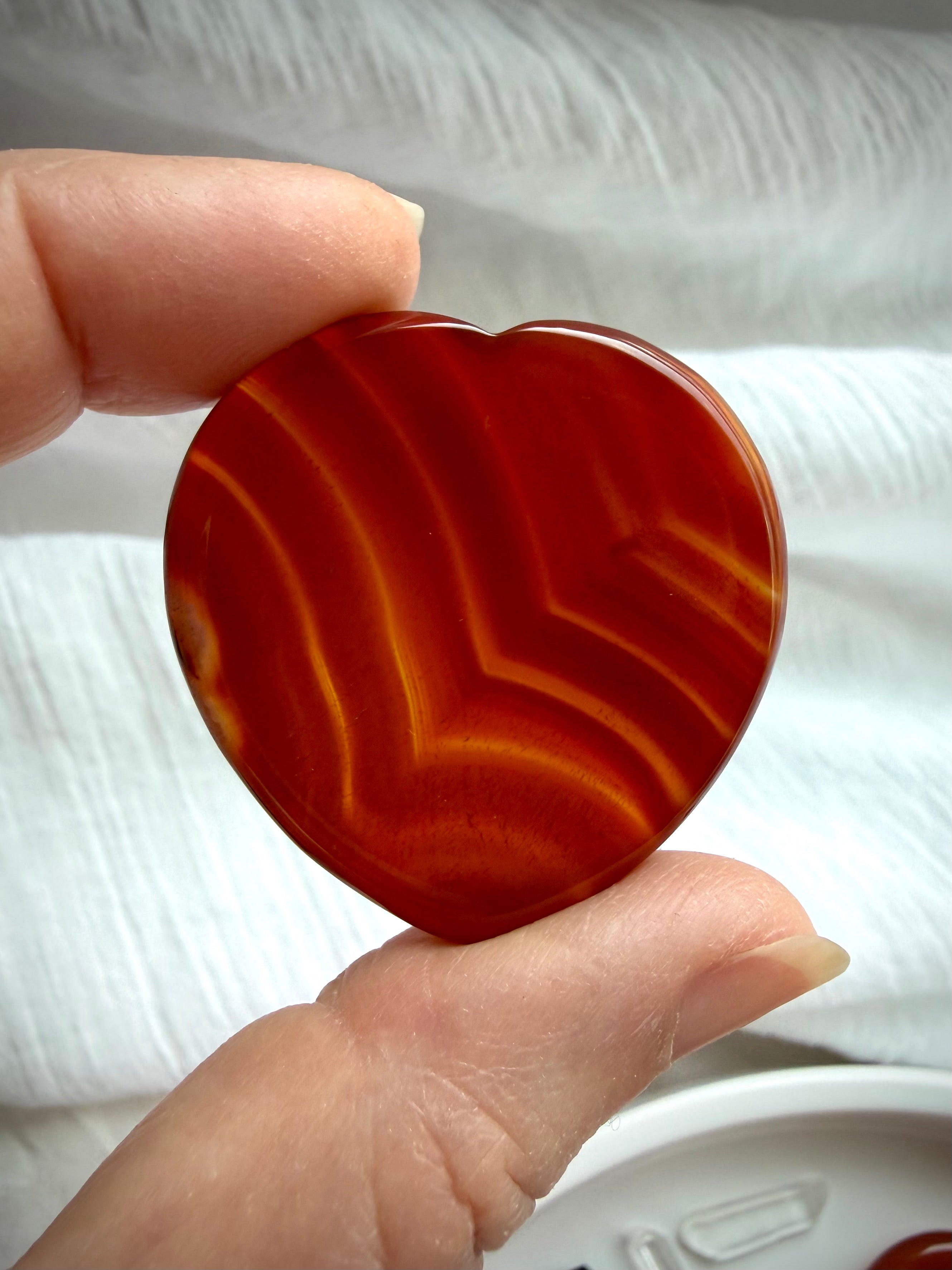 Translucent Carnelian heart worry stone with vivid red-orange banding and polished thumb indentation