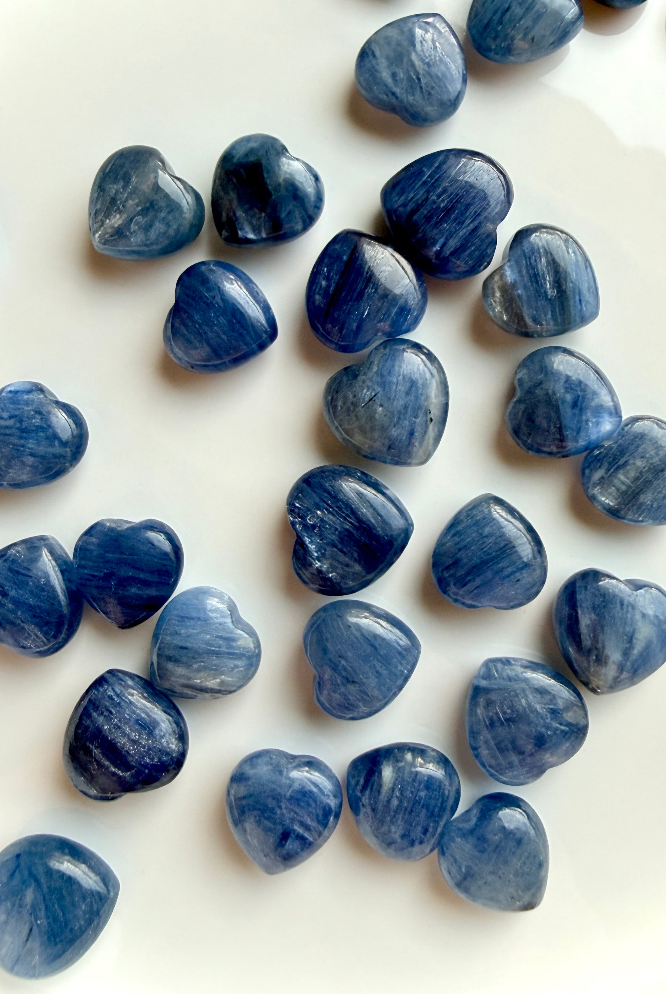 Scattered mini Blue Kyanite heart crystals on white background showing natural variation in color, shimmer and inclusions