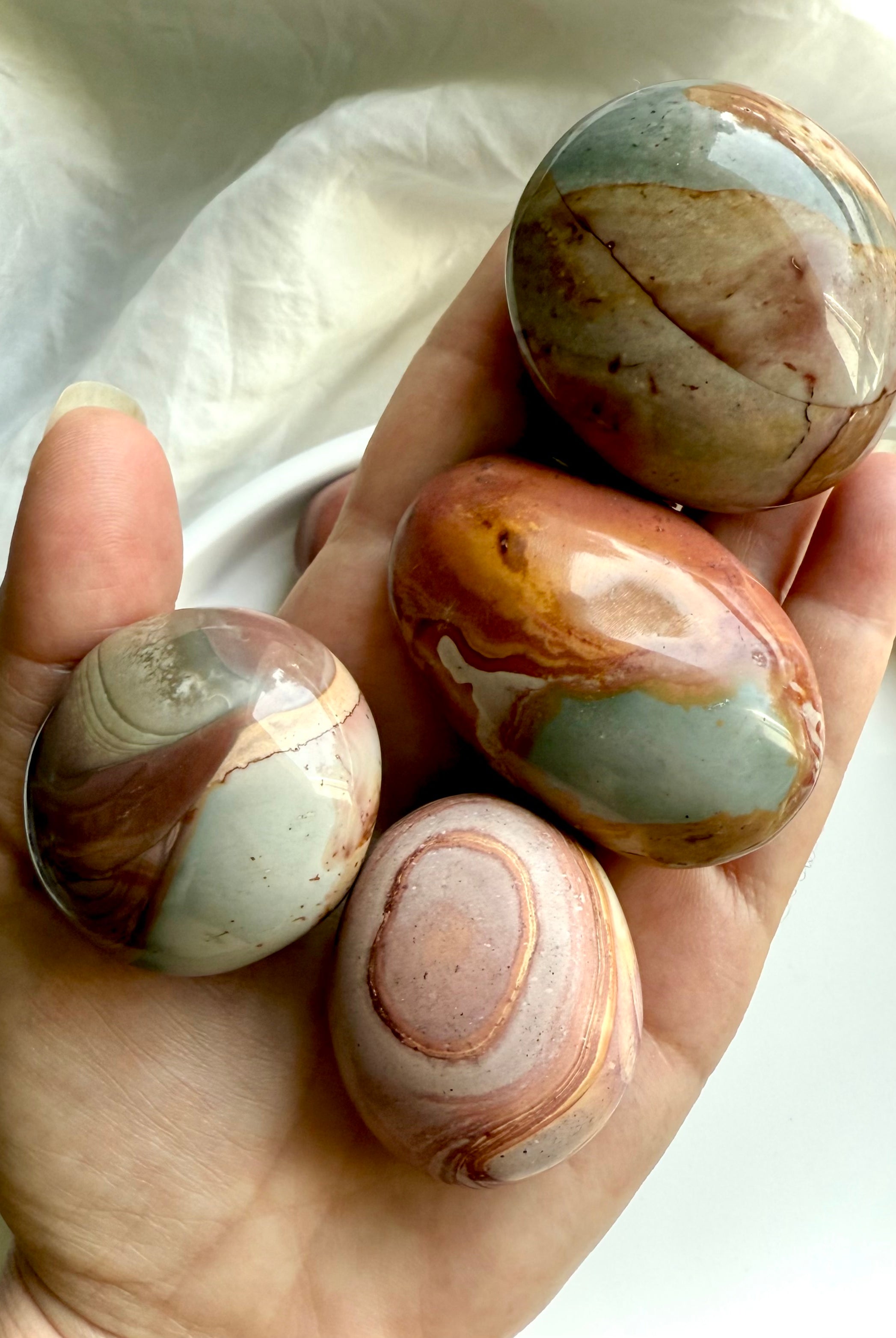 Polychrome Jasper palm stones shown in hand, highlighting size variety & earthy, grounding energy.