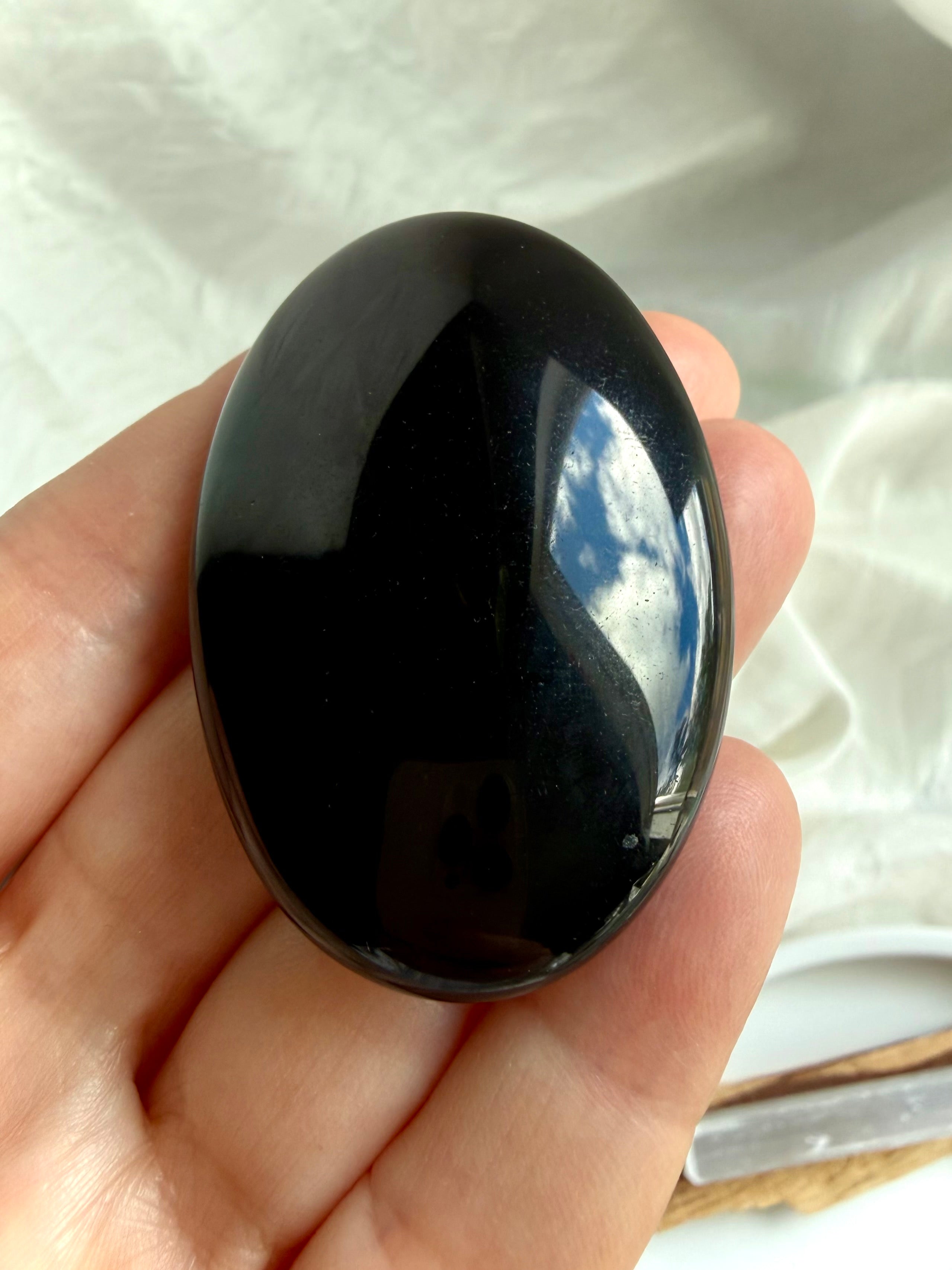 Close-up of polished Black Obsidian palm stone with reflective mirror-like finish and natural volcanic glass beauty
