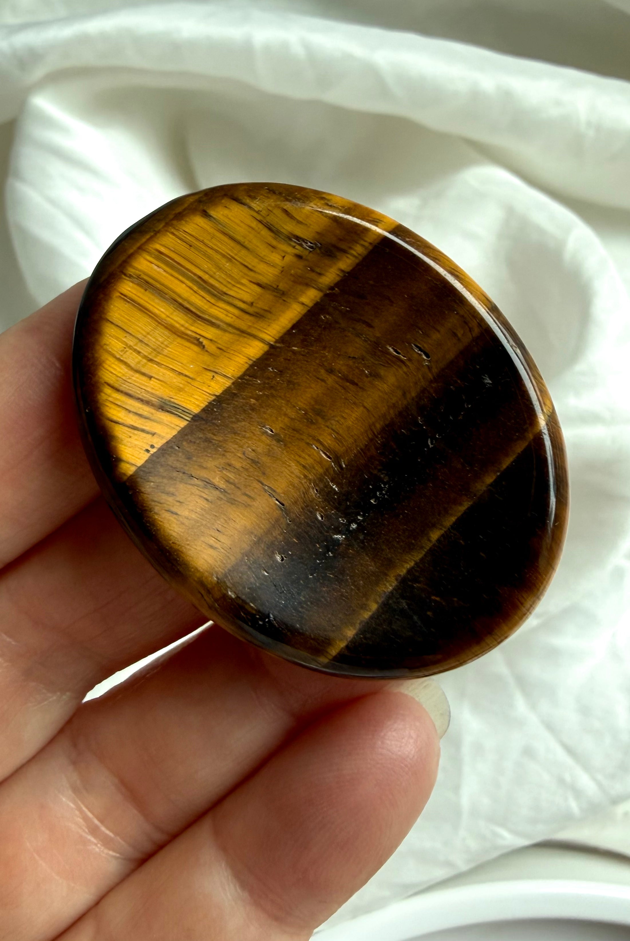 close-up tiger’s eye worry stone in hand with strong chatoyancy flash, grounding crystal for solar plexus confidence and clarity