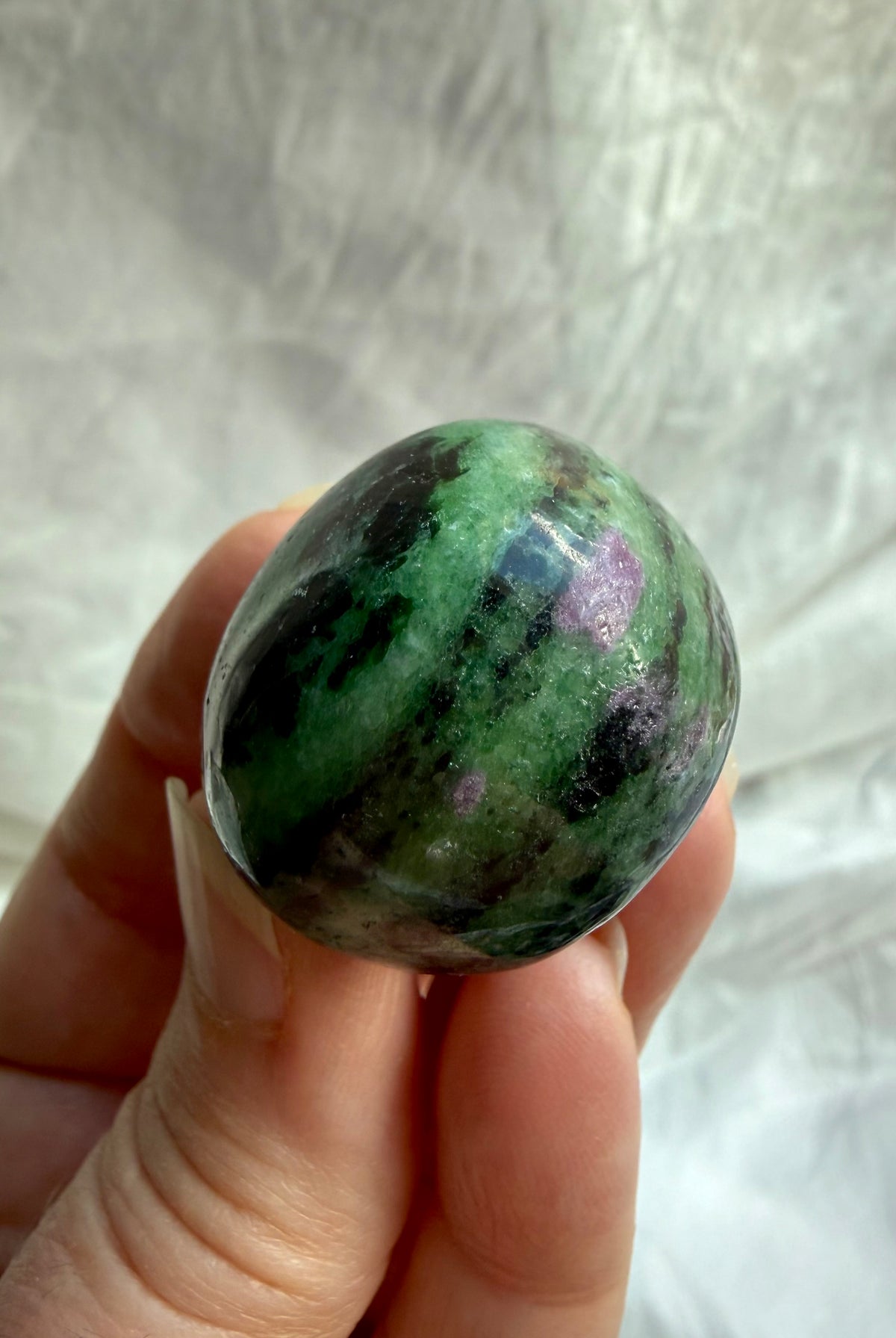 Close-up of polished Ruby Zoisite gemstone showing vibrant green and pink mineral formations with natural black inclusions