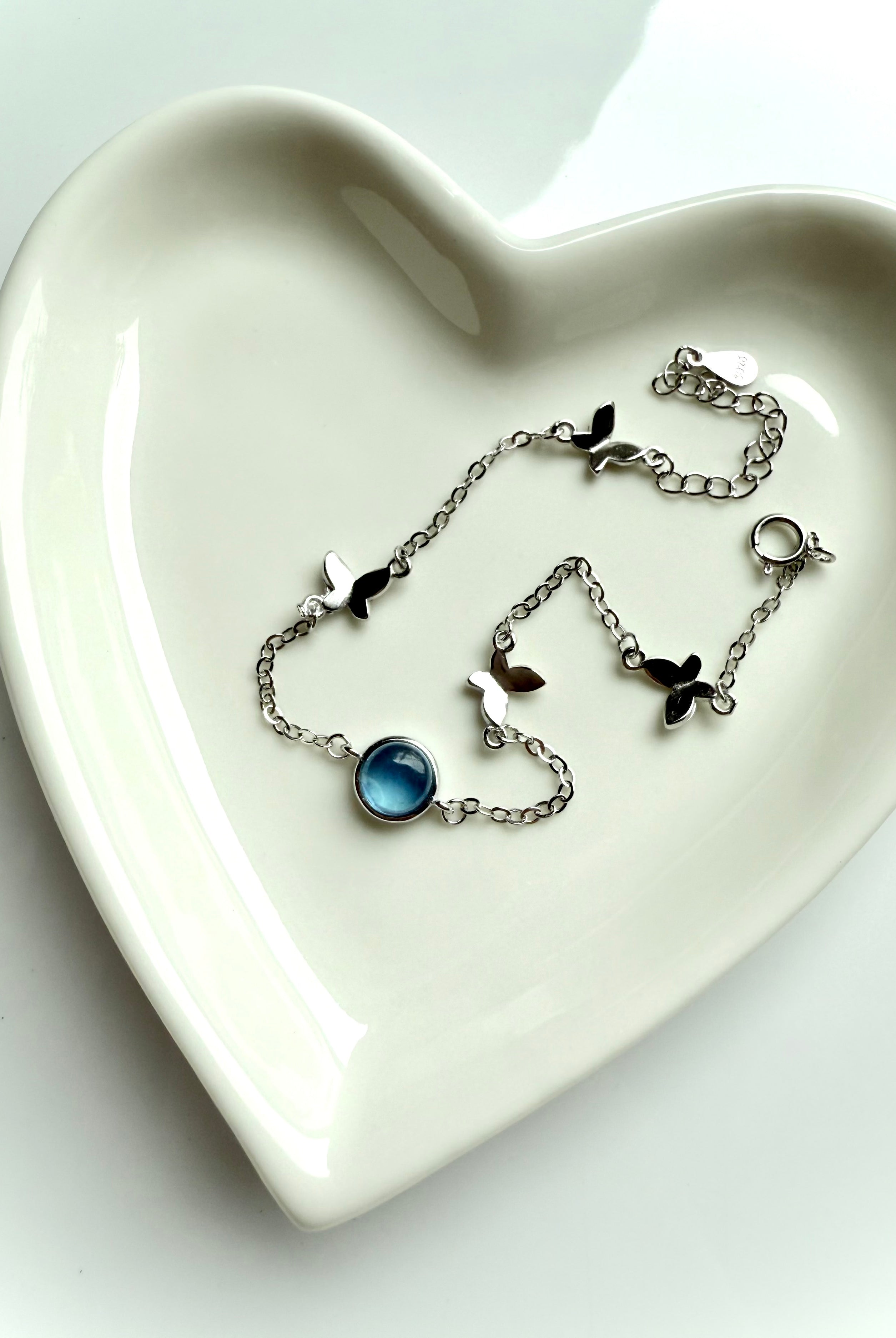 Dainty sterling silver aquamarine butterfly bracelet with heart chakra energy, styled in heart-shaped dish for gift-ready presentation