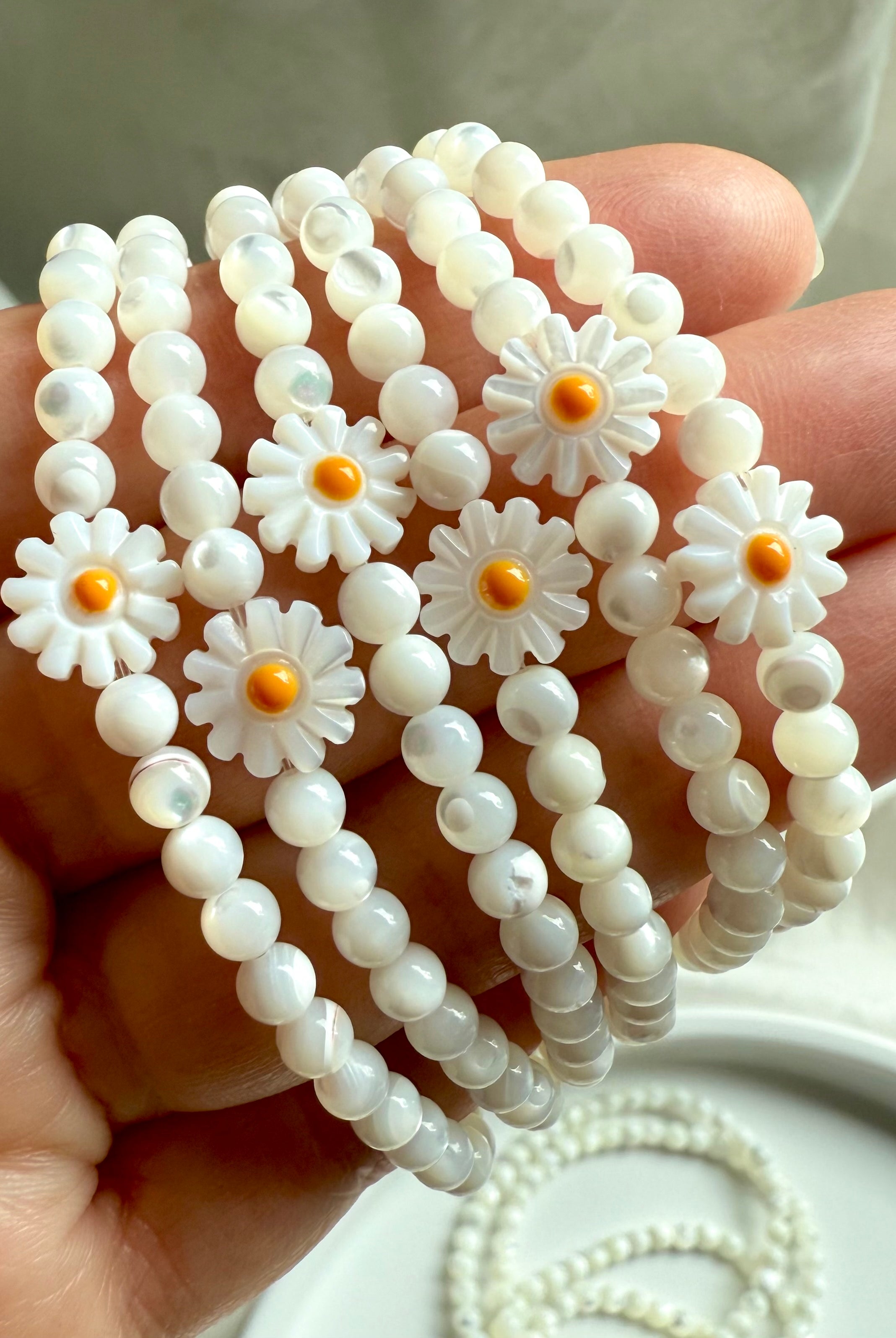 Hand holding boho-style Mother of Pearl daisy bracelets with natural white gemstone beads and carved flower accents, stacked for a whimsical and lighthearted crystal jewelry look