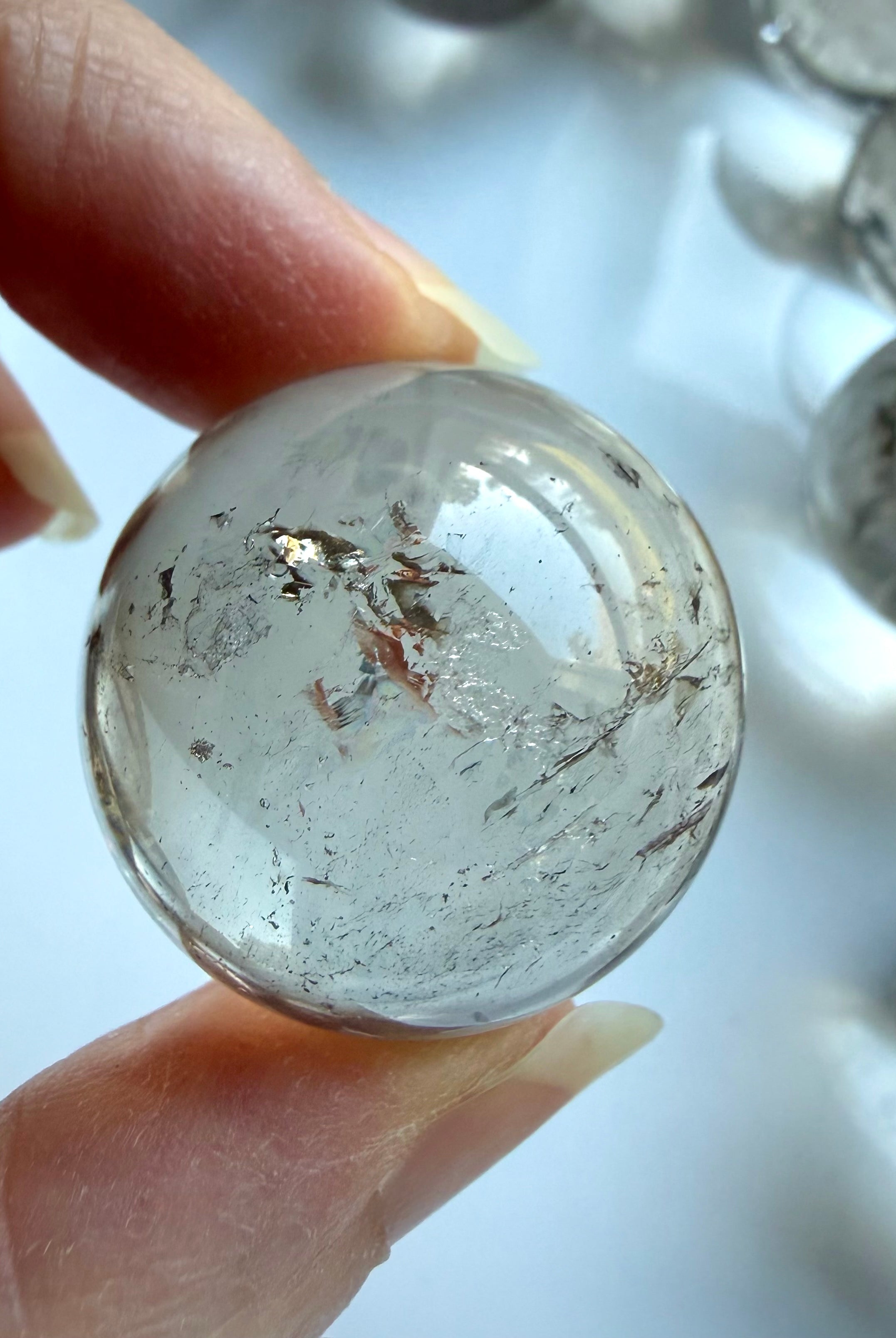 Small Smoky Quartz sphere held between fingers showing soft translucent smoky color and inclusions