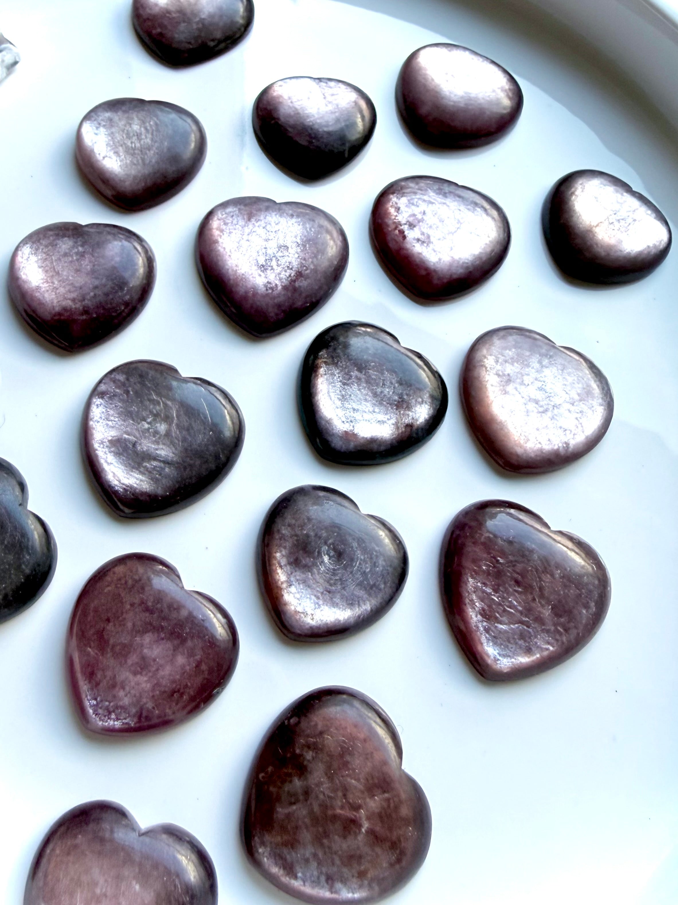 Gem Lepidolite crystal hearts on white tray showing lavender to plum tones with natural mica shimmer and polished surfaces