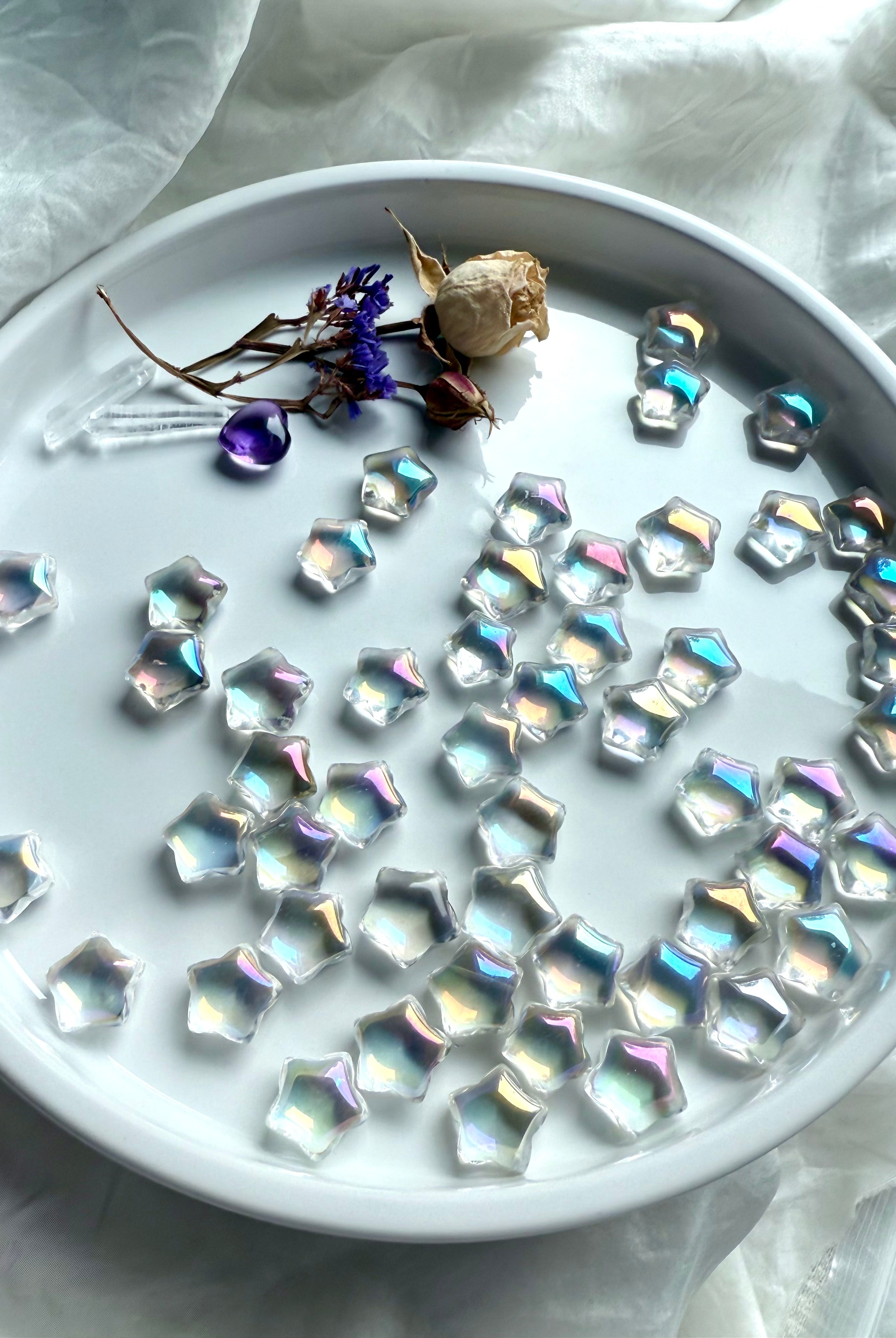 Opalescent mini aura quartz stars with rainbow sheen displayed on white tray with dried flowers, amethyst heart, and quartz points — healing crystals for universal chakra balance.
