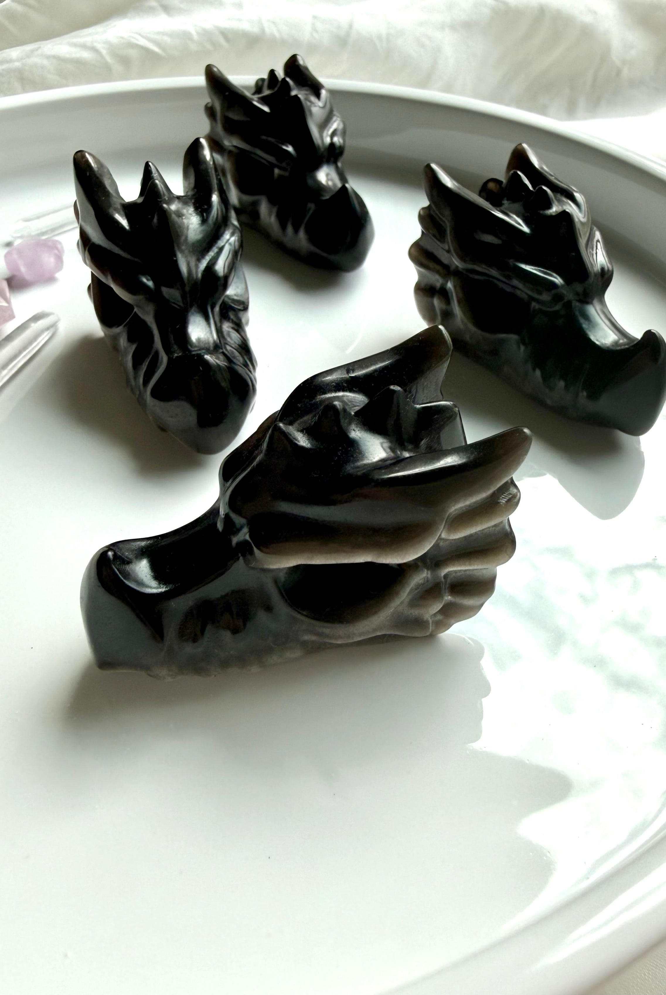 four silver sheen obsidian dragon carvings on neutral background, grounding crystals for protection and energetic clearing