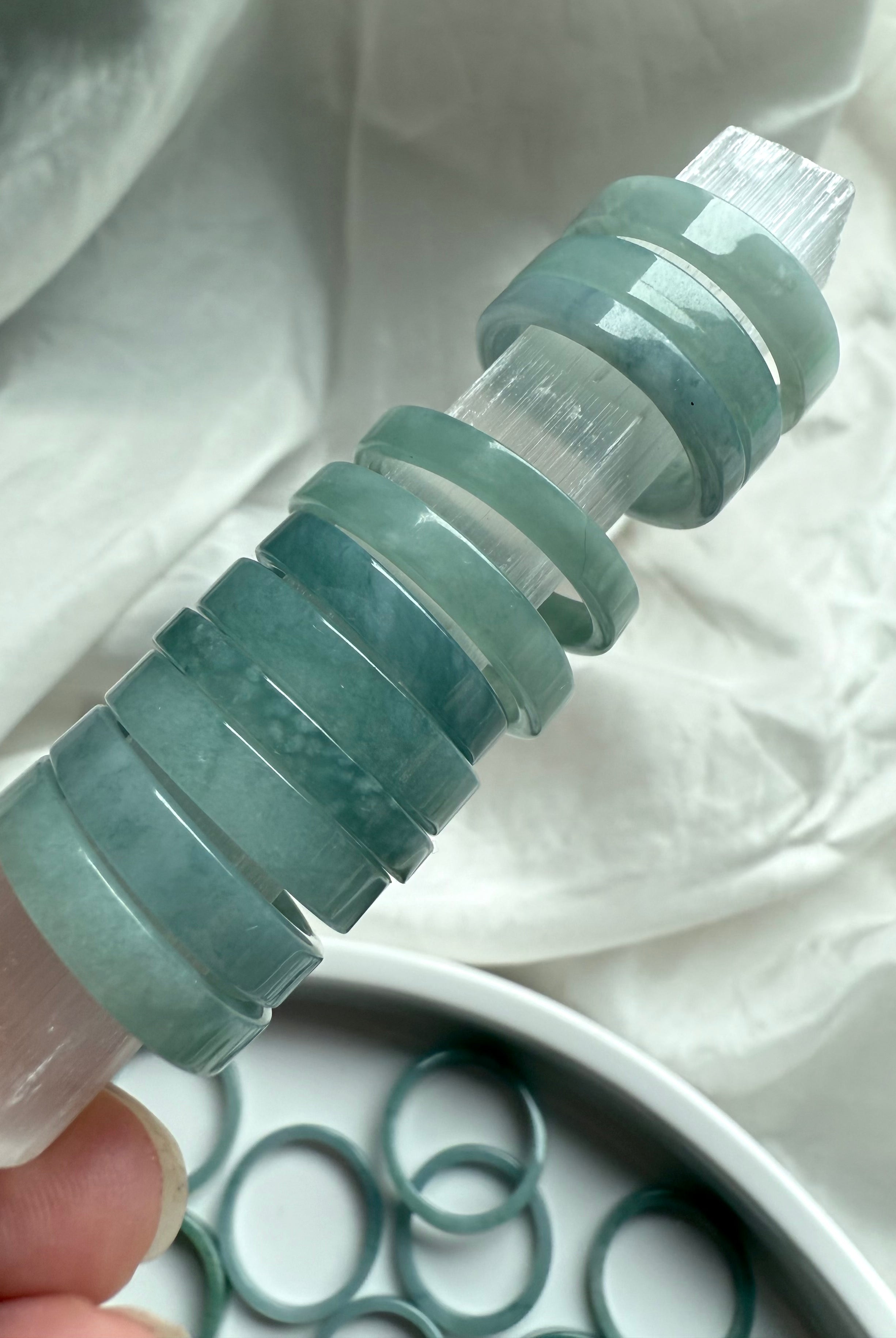 Flat band jade rings displayed on a selenite wand to showcase translucency and soft polish