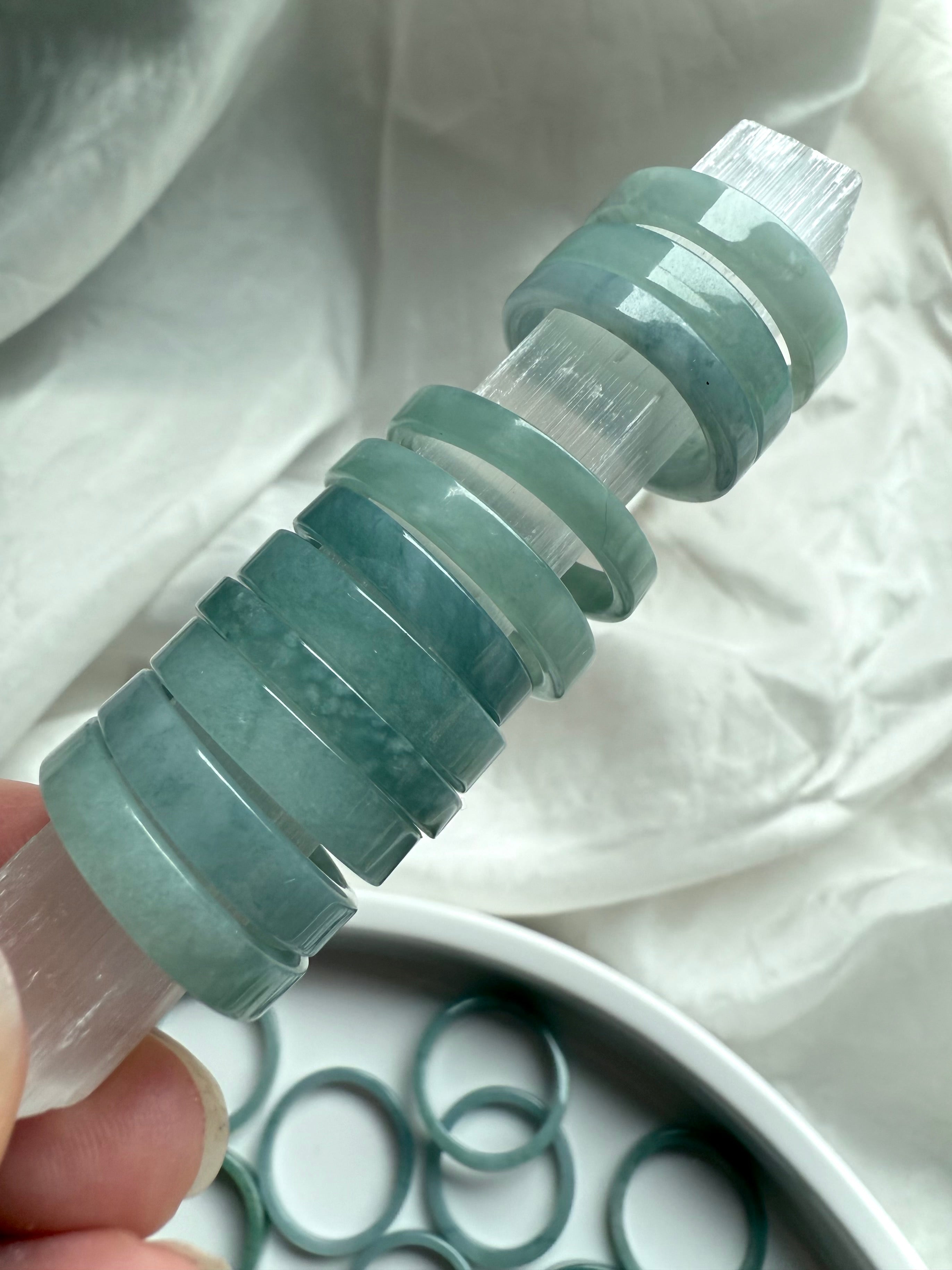 Flat band jade rings displayed on a selenite wand to showcase translucency and soft polish
