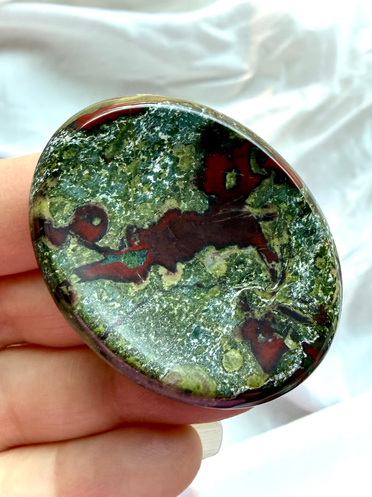 Dragon Blood Stone worry stone held in hand, showing rich green Epidote, burgundy-red Piemontite and natural mineral patterns