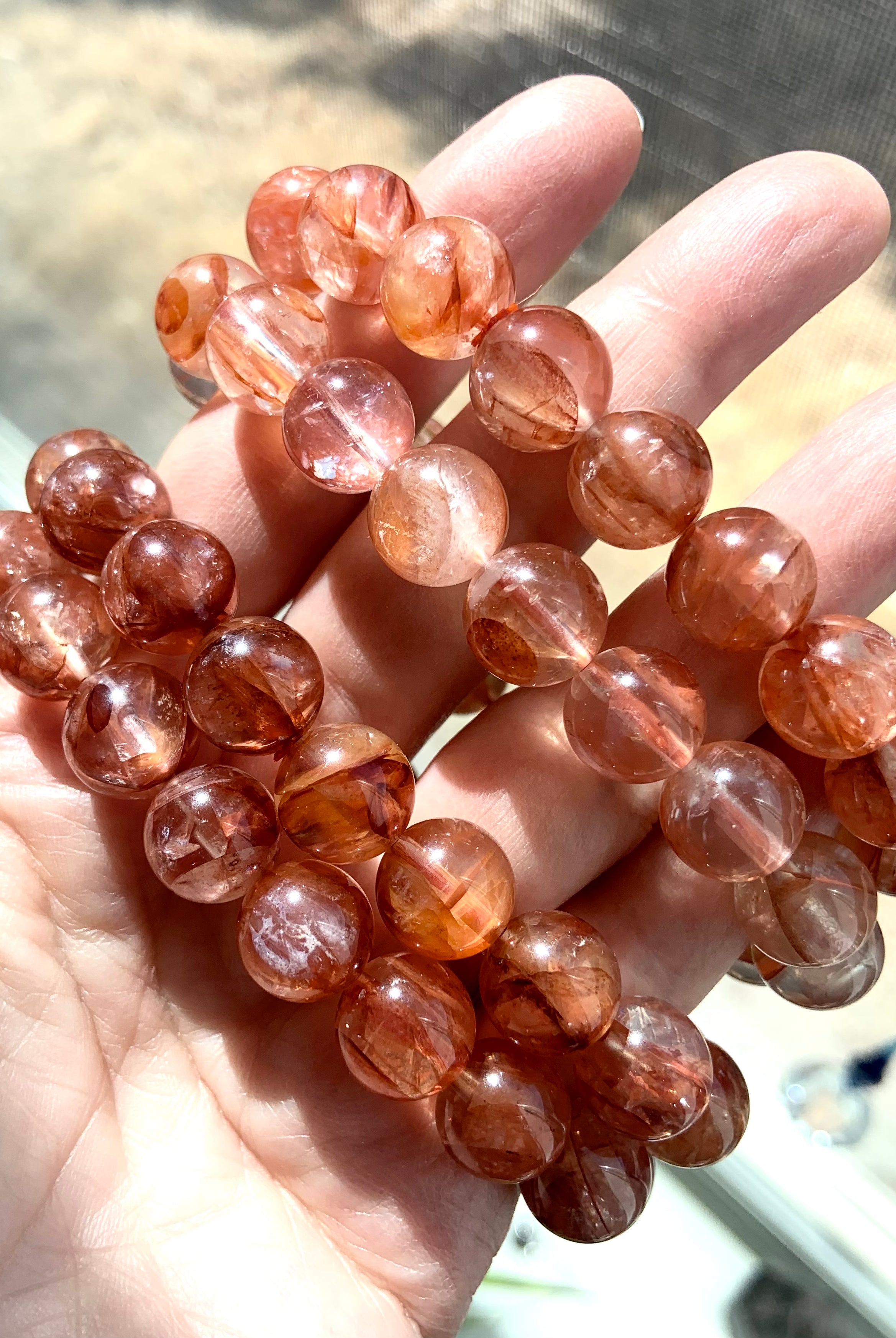 Four Fire Quartz bracelets held on hand, showing a mix of light and dark red quartz bead tones for variety in color and energy