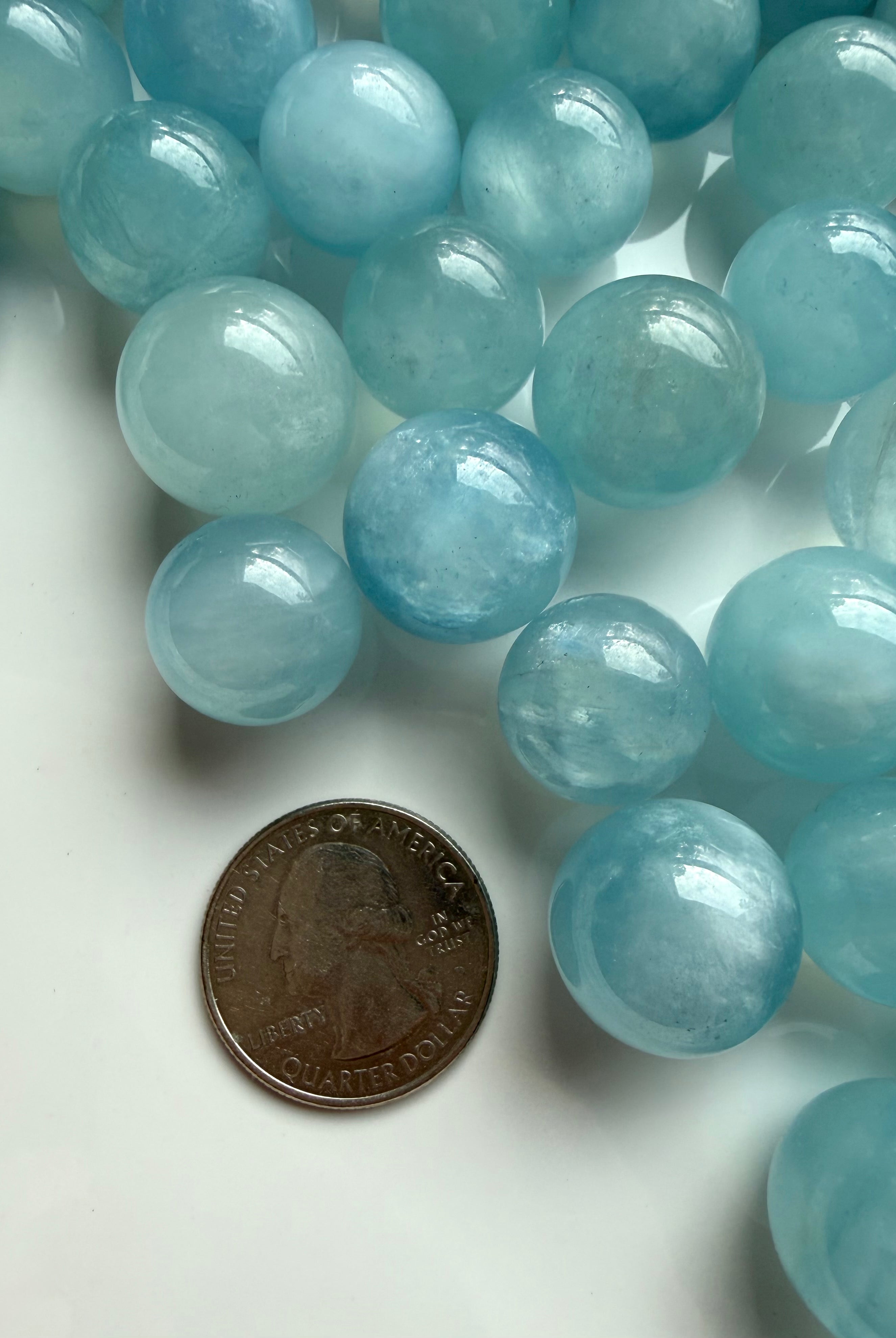 Mini Aquamarine sphere beside coin for scale – small blue March birthstone crystal ball