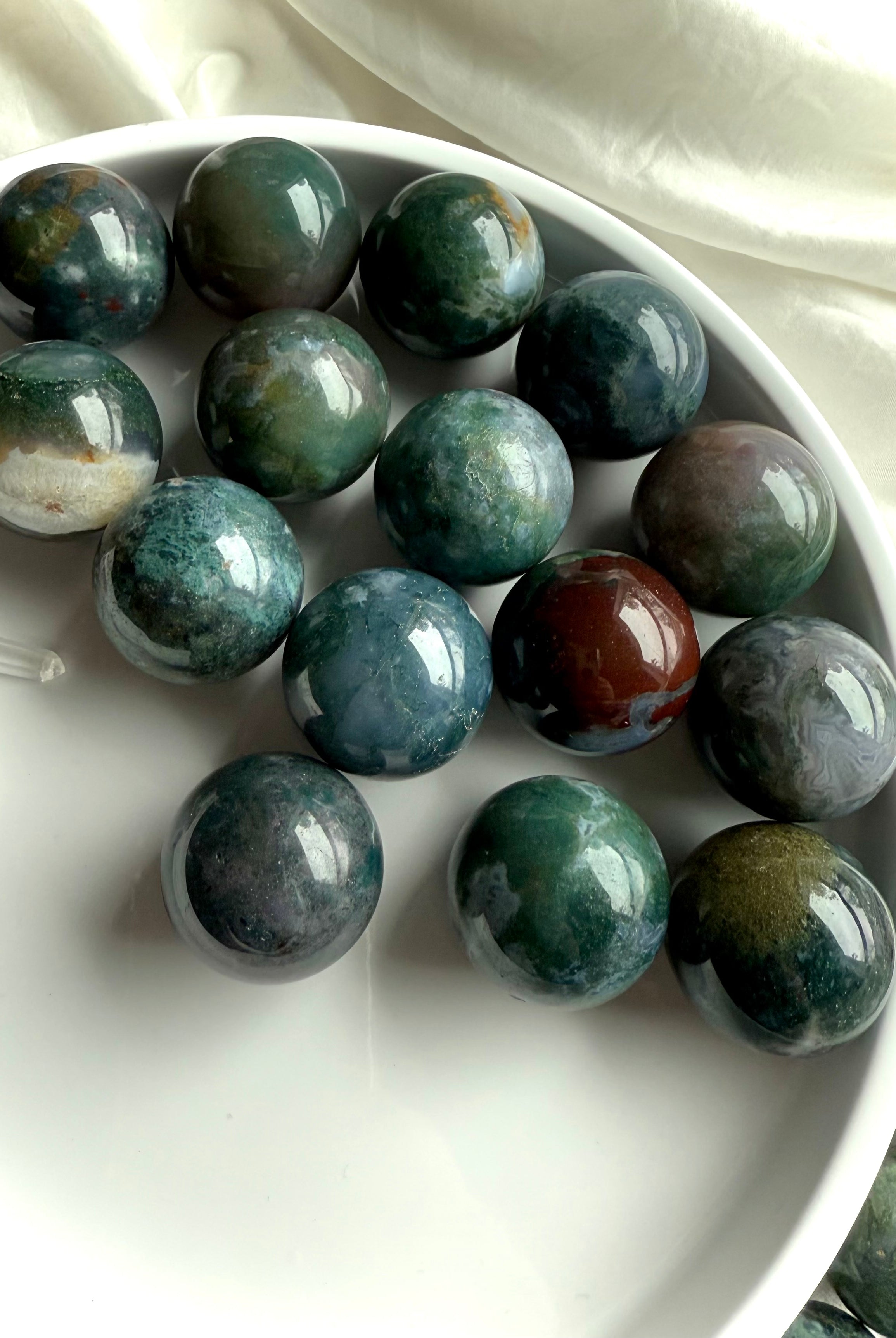 Colorful moss agate mini spheres shown on a white plate, photographed in natural light