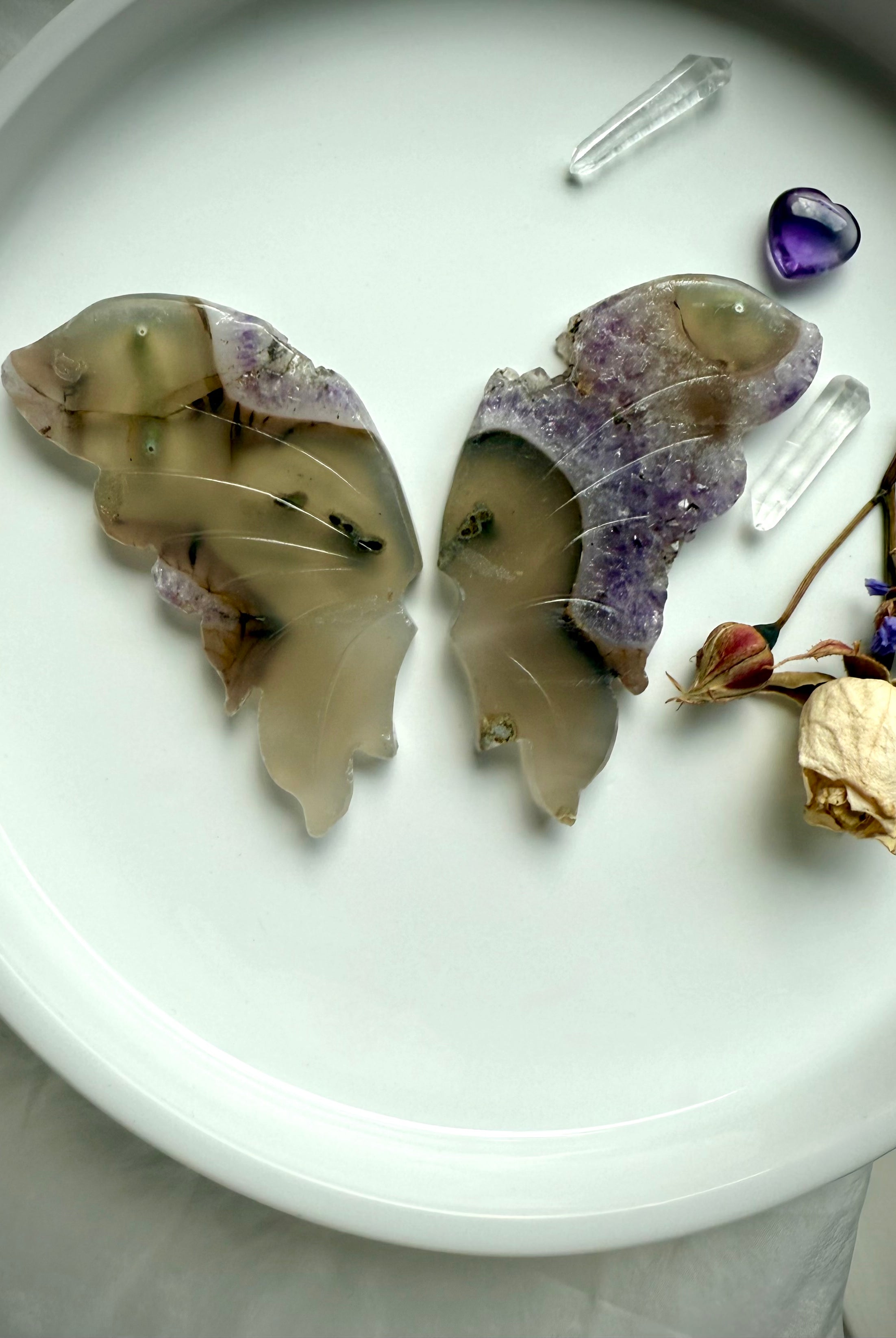 Carved agate butterfly wings with natural amethyst druzy on white tray, shown with quartz points and dried flowers.