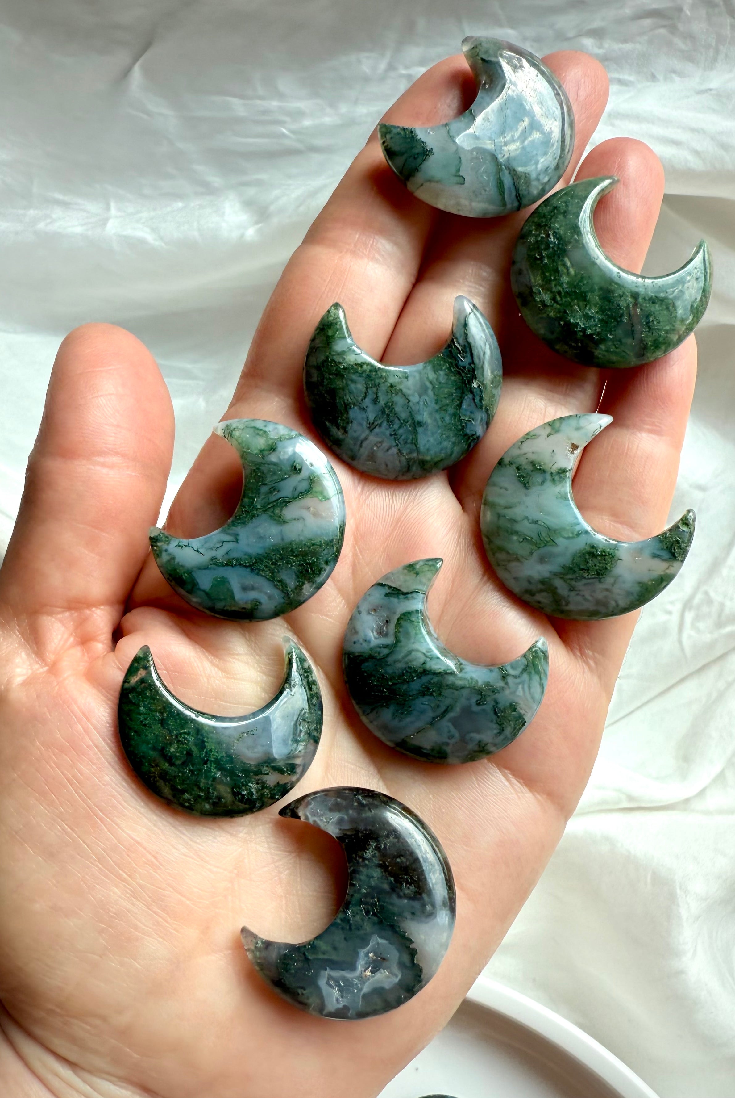Array of Moss Agate crescent moon crystals in hand showing size and earthy green color.