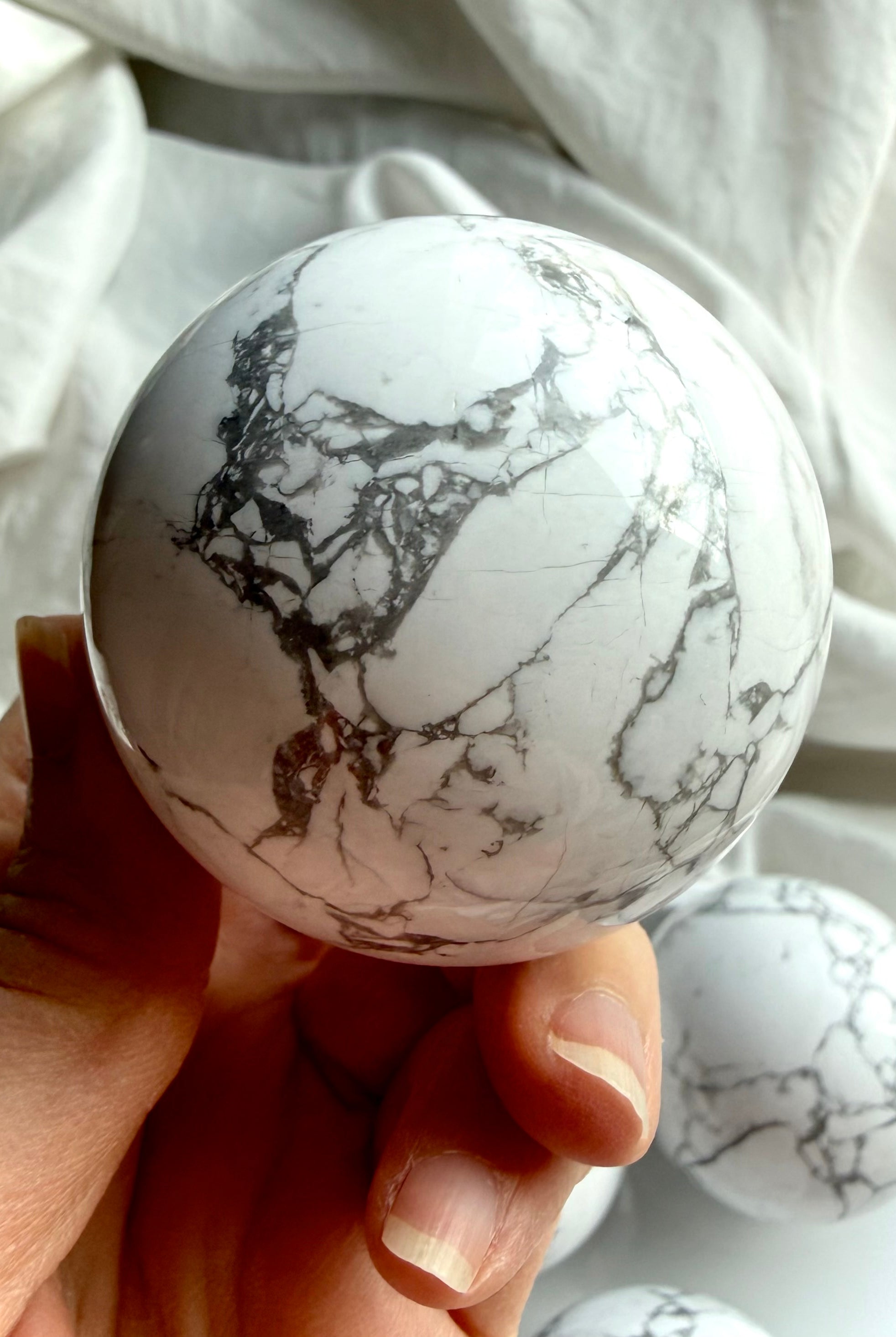 Polished Howlite sphere held in hand highlighting natural marbled pattern and glossy finish, soothing crystal for sleep and emotional balance