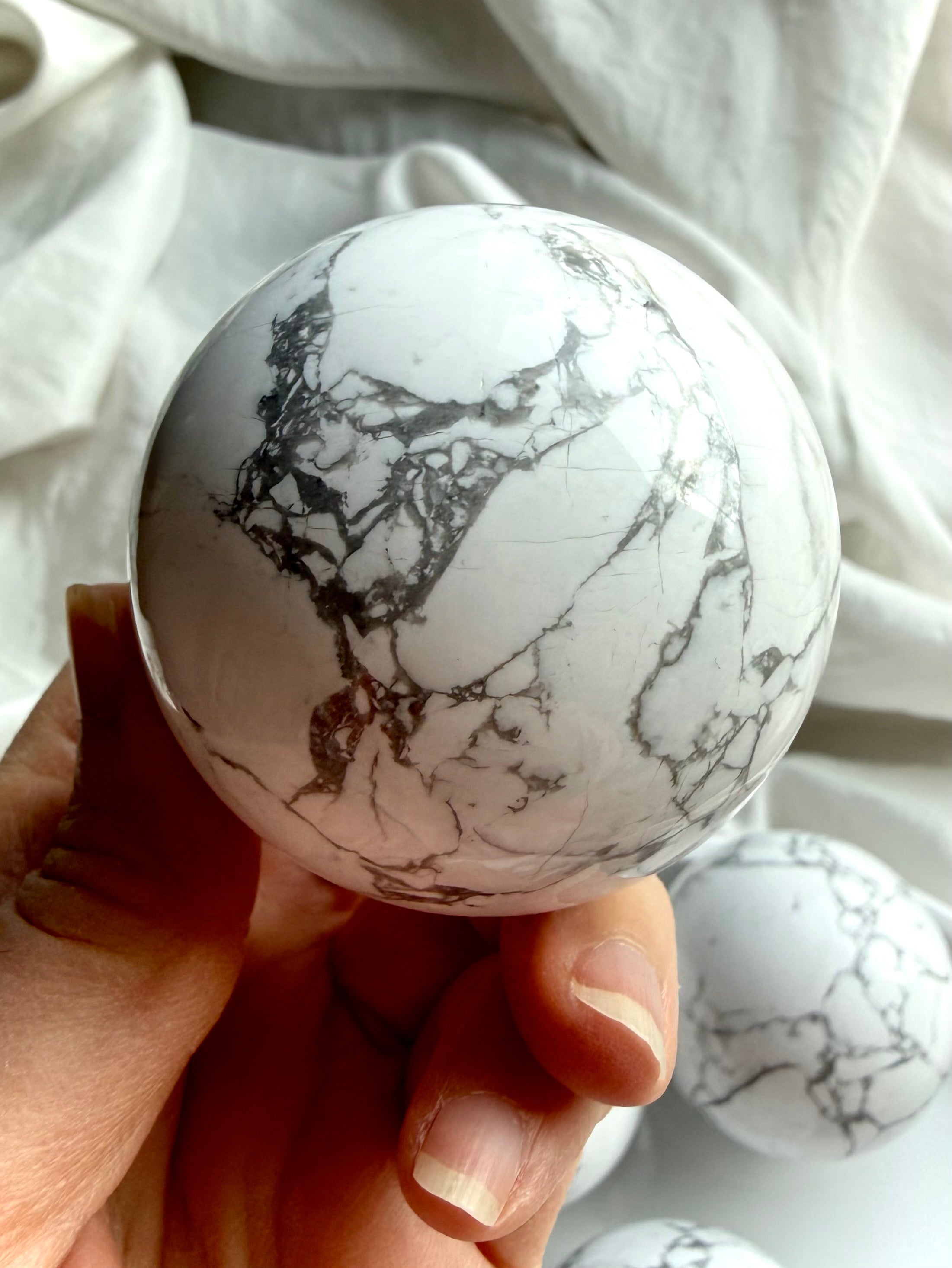 Polished Howlite sphere held in hand highlighting natural marbled pattern and glossy finish, soothing crystal for sleep and emotional balance