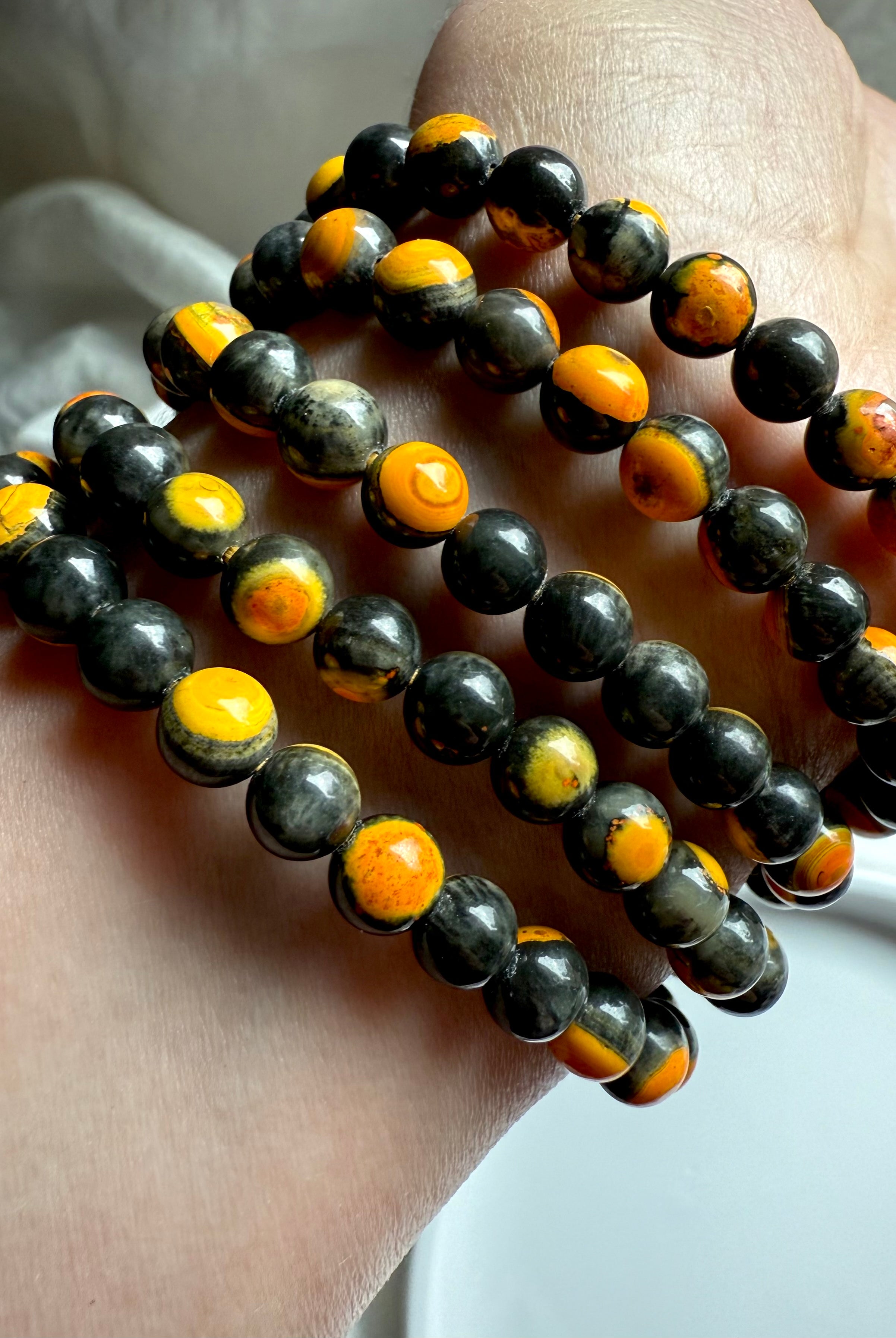 Five stacked bumblebee jasper bracelets laid out in a curved display, glowing yellow hues in radiant orbicular patterns