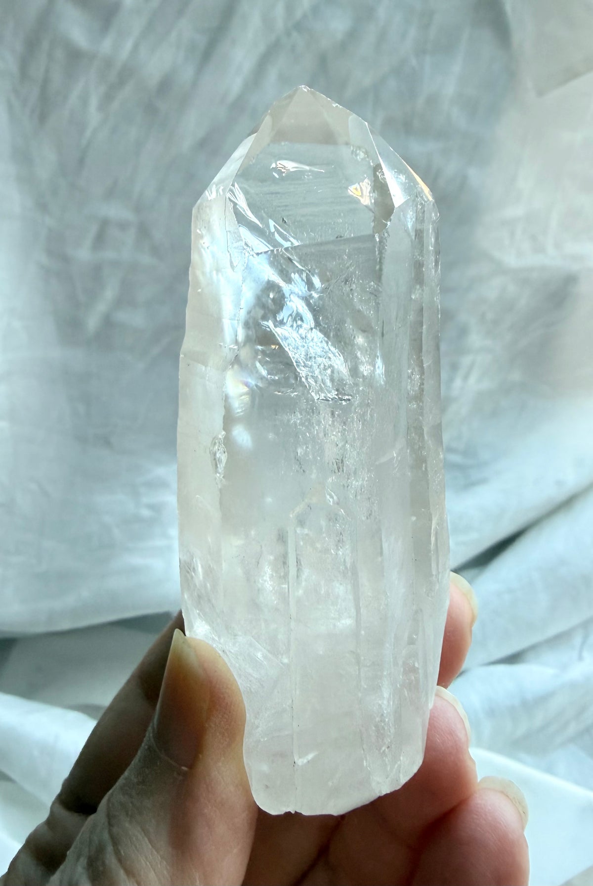 Brazilian Lemurian Quartz point held in hand with natural termination, ladder lines, internal veils, and inclusions